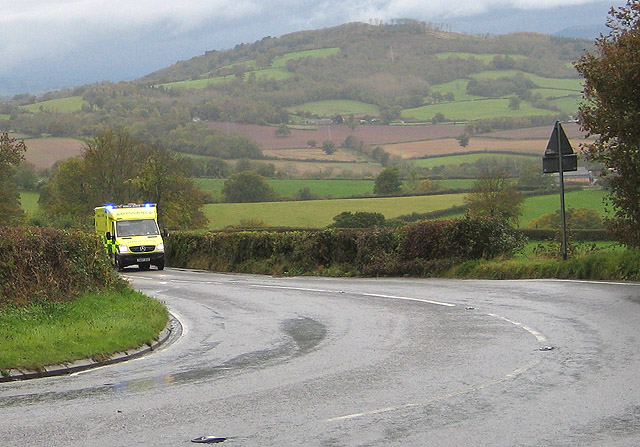 An ambulance with its blue lights flashing coming along a country road, the everyday siren whose pitch drops as it passes you