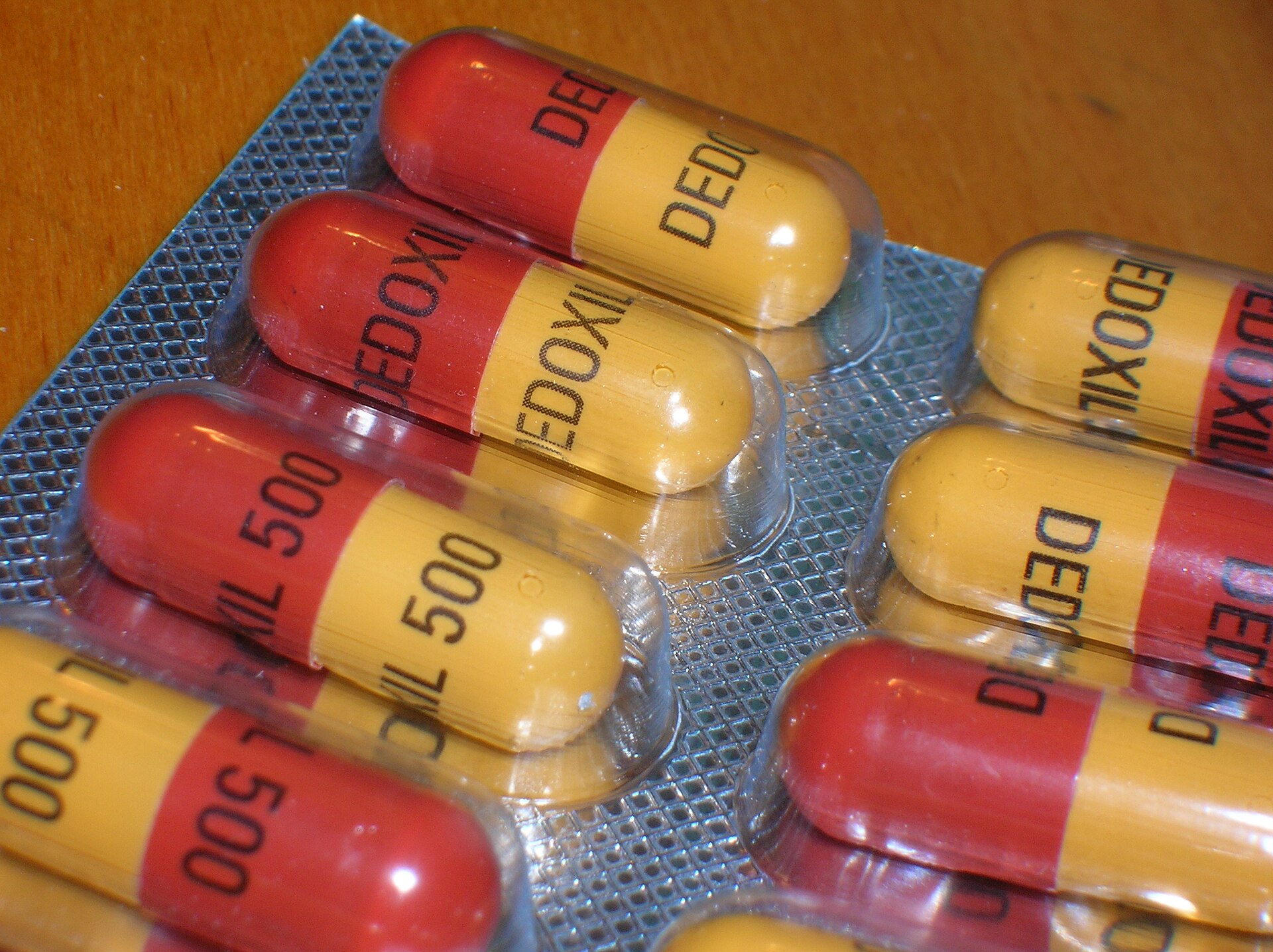 Red and yellow antibiotic capsules sealed in a foil blister pack on a wooden table.