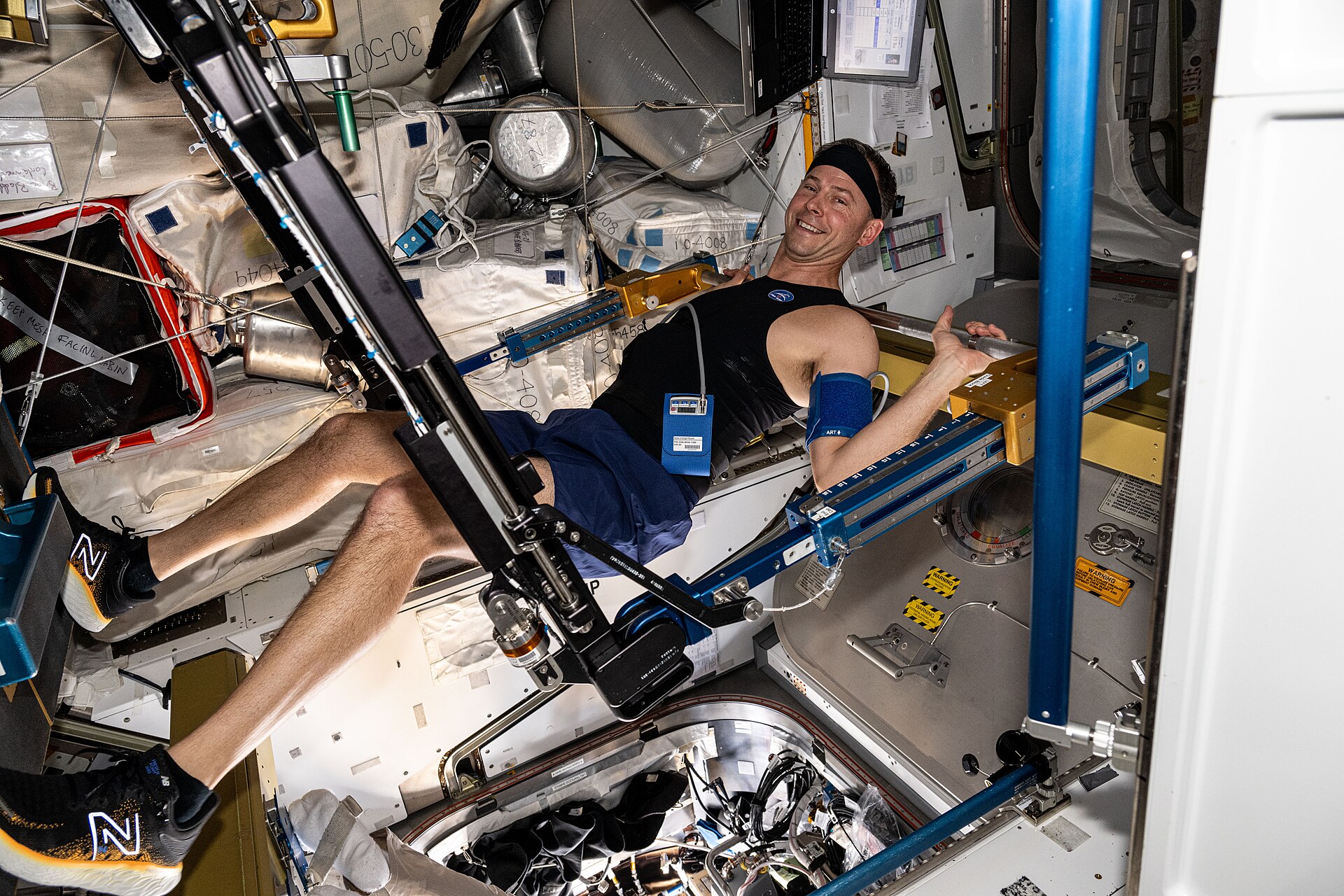 An astronaut working out on the space station's resistance machine, pushing against a bar with both legs
