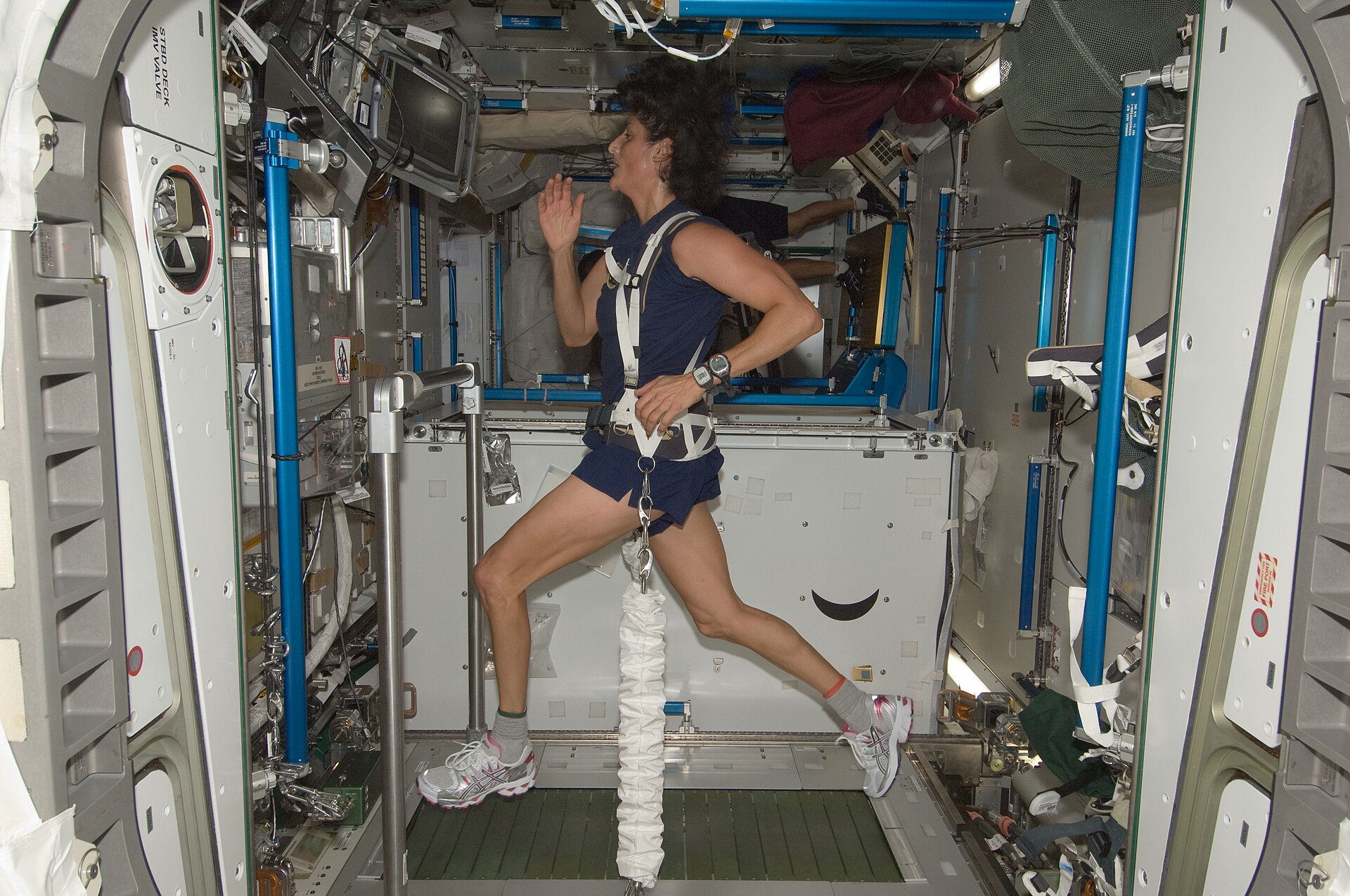 An astronaut running on the space station treadmill, held down onto the belt by a harness and elastic cords