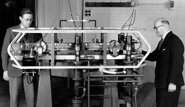 Two scientists beside the first caesium atomic clock at Britain's National Physical Laboratory, the kind of clock accurate enough to catch time itself running slow
