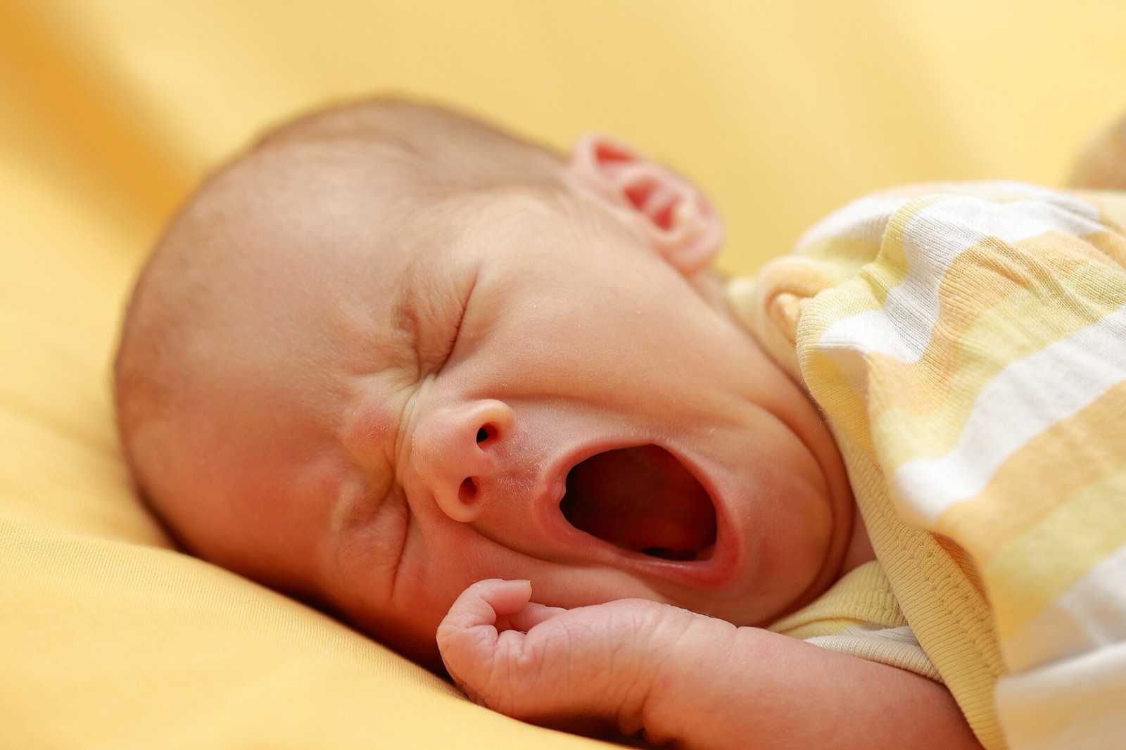 A newborn baby yawning widely, eyes scrunched shut.