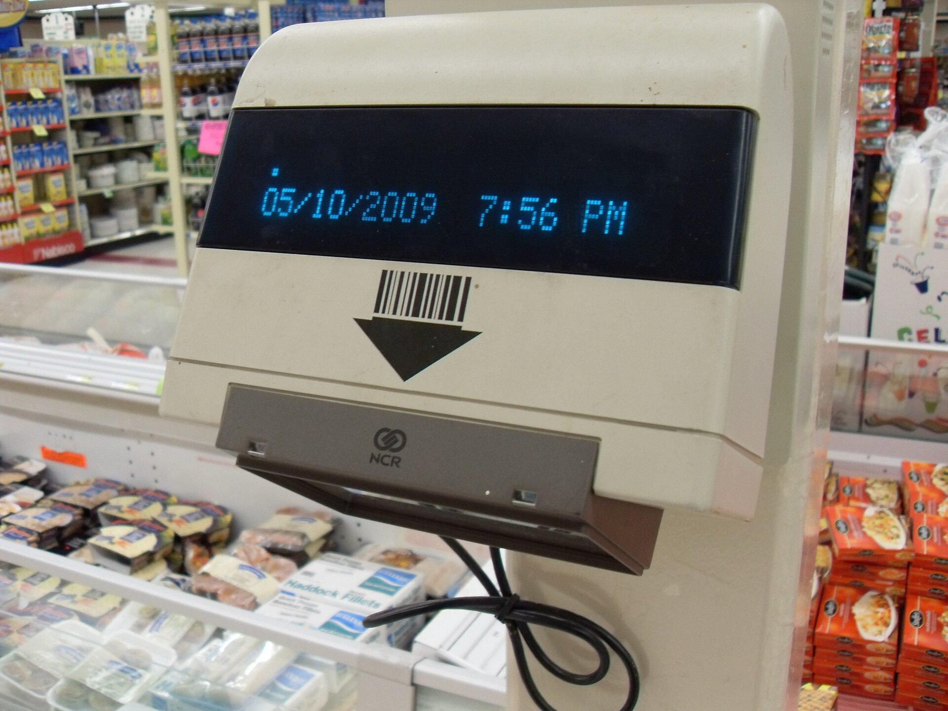 A supermarket price scanner with a barcode symbol and an arrow pointing down to the scanning window