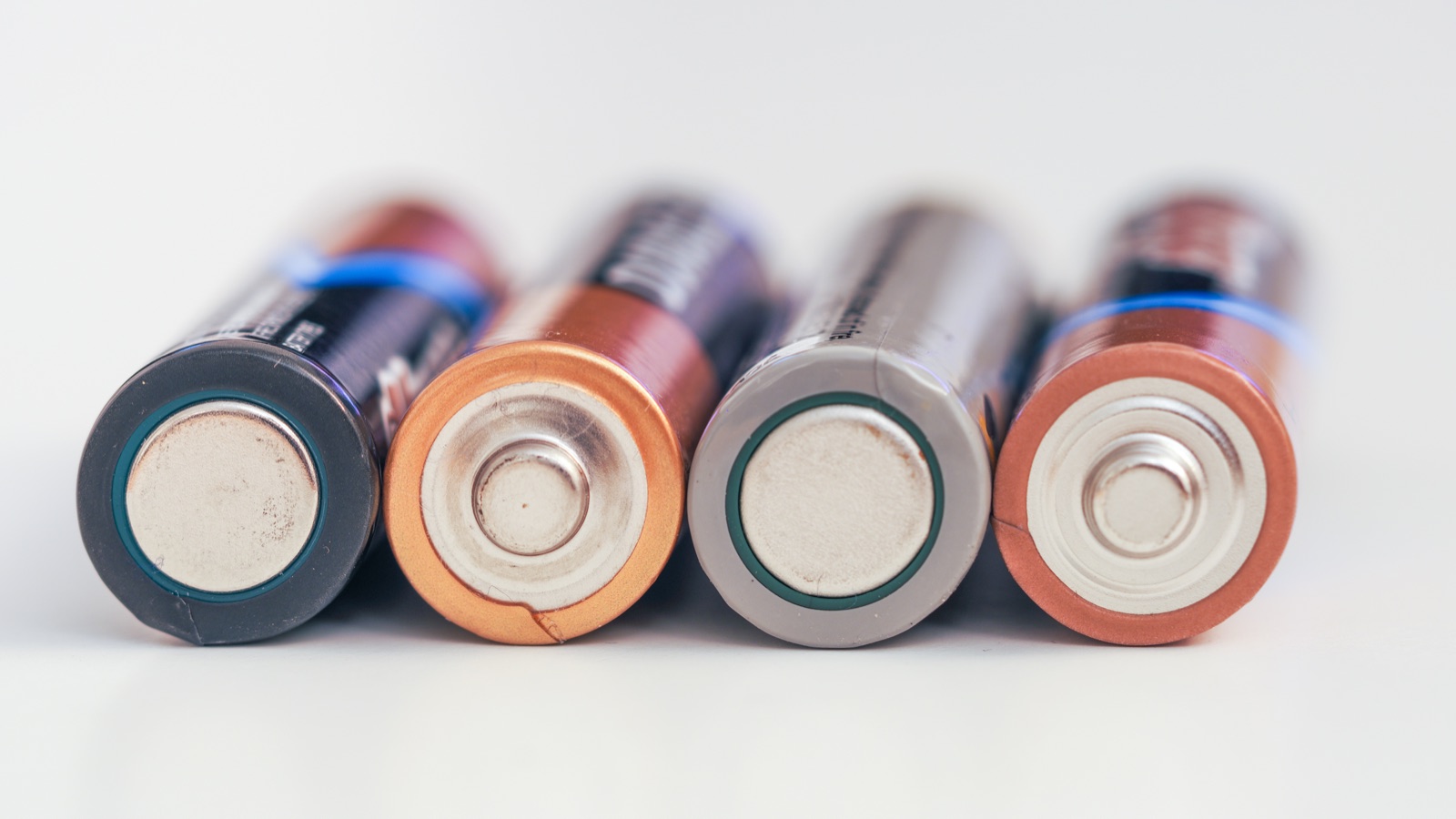 Four AA batteries lying side by side, seen end on, so the raised metal bump of the positive end on each one is clearly visible