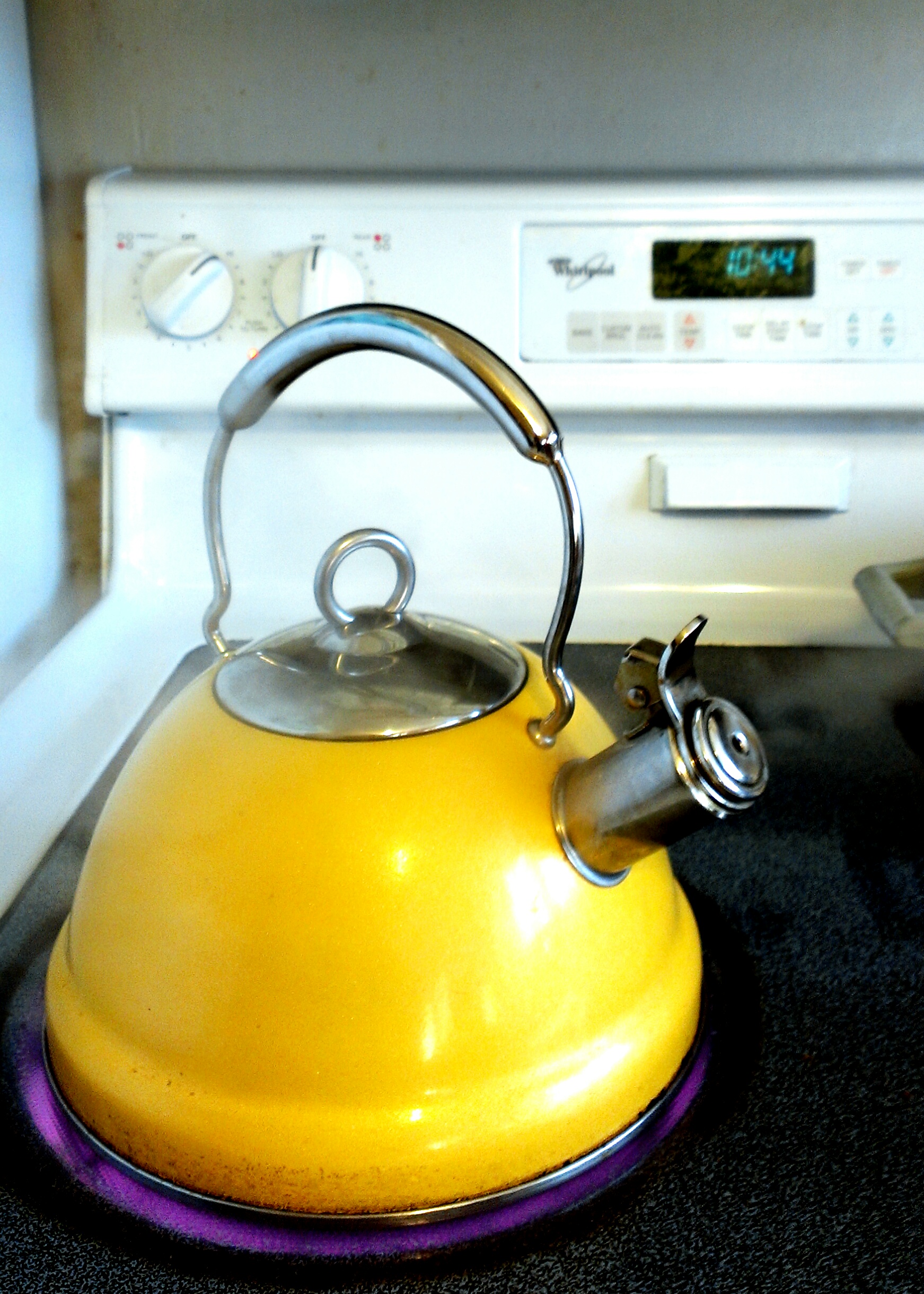 A yellow stovetop kettle sitting on a glowing hob ring.