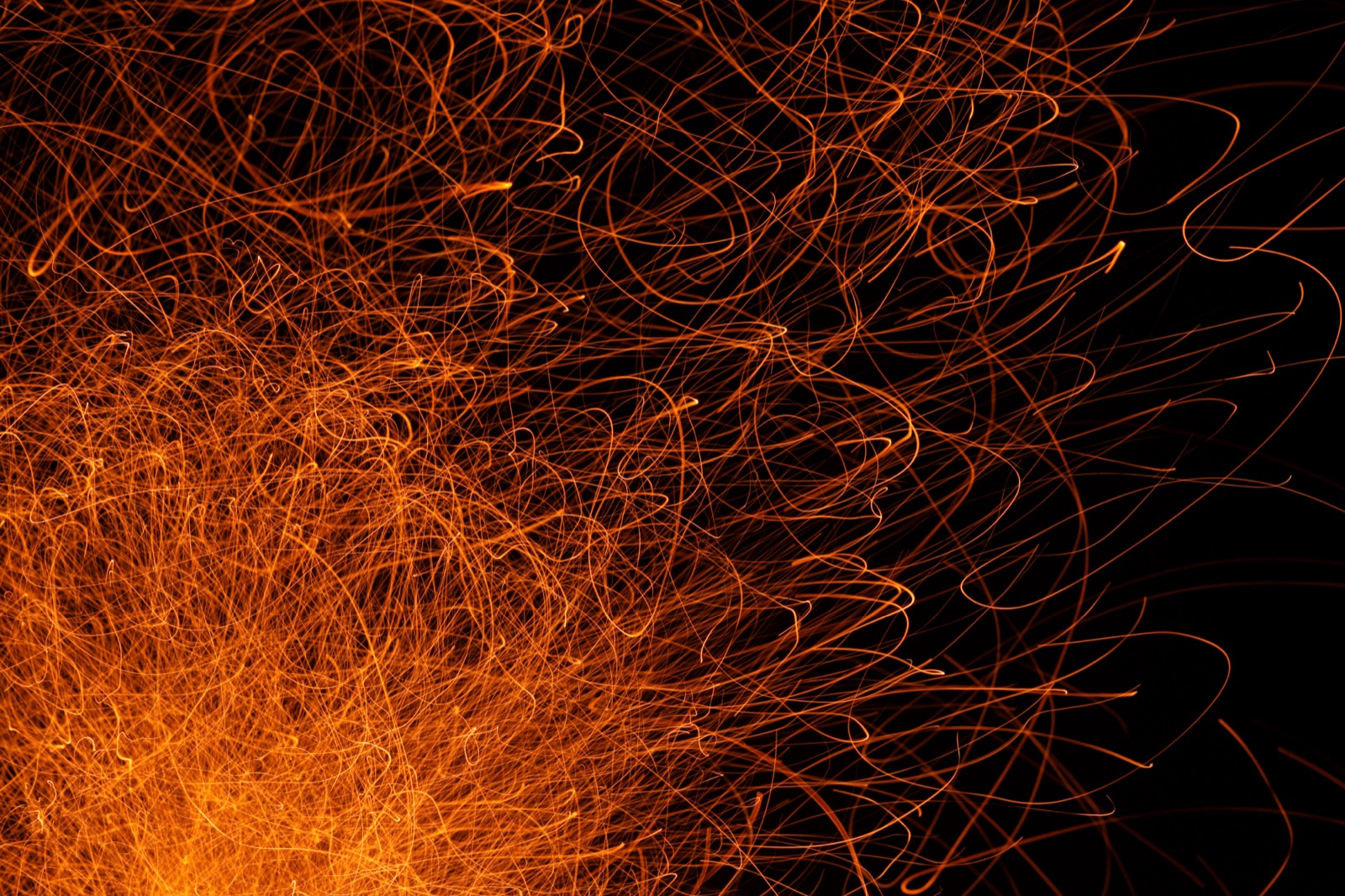 Glowing orange sparks streaming from a campfire at night, energy stored in chemical bonds released as heat and light.