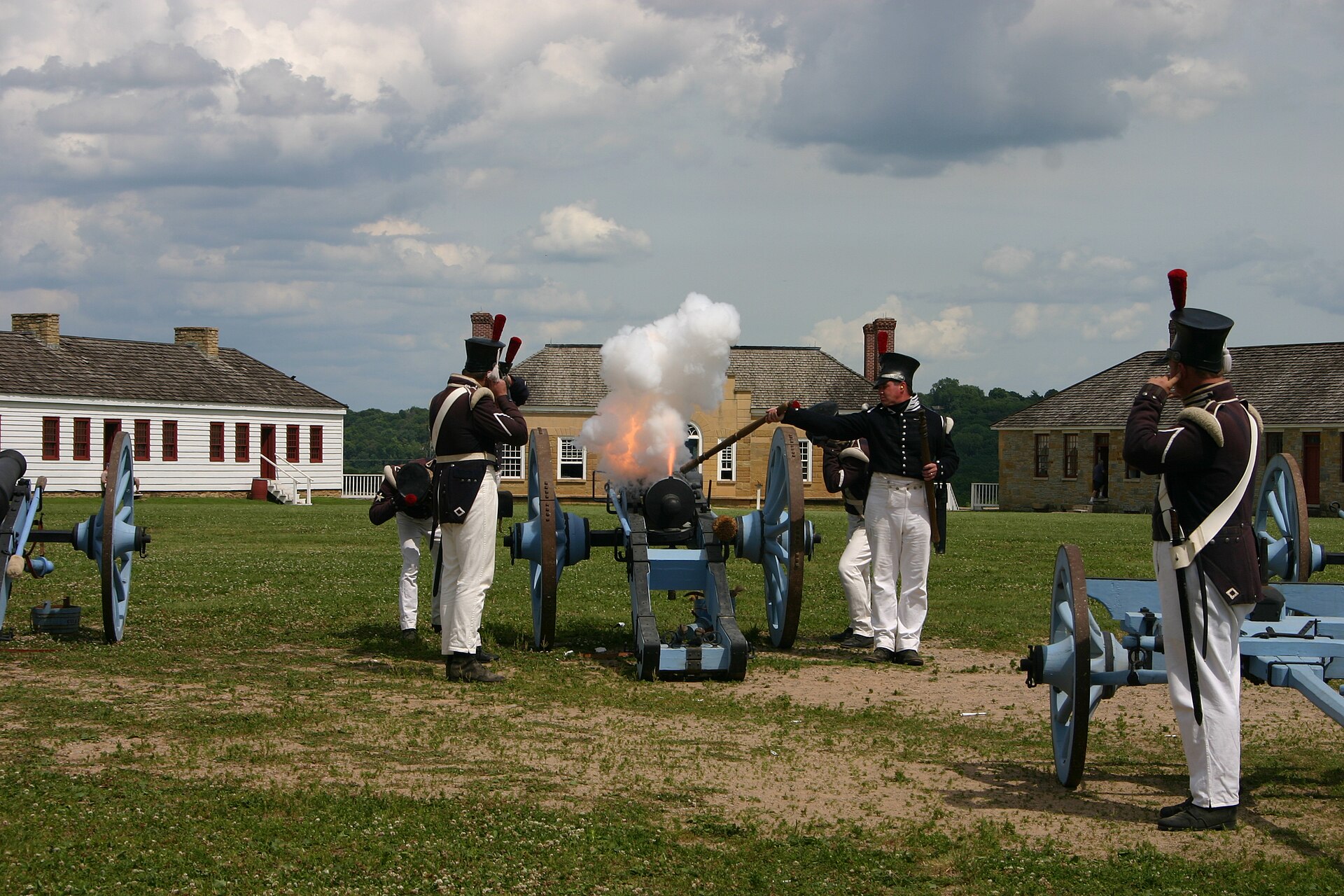 A historic cannon being fired at a fort, with a burst of flame and a cloud of white smoke leaving the muzzle.