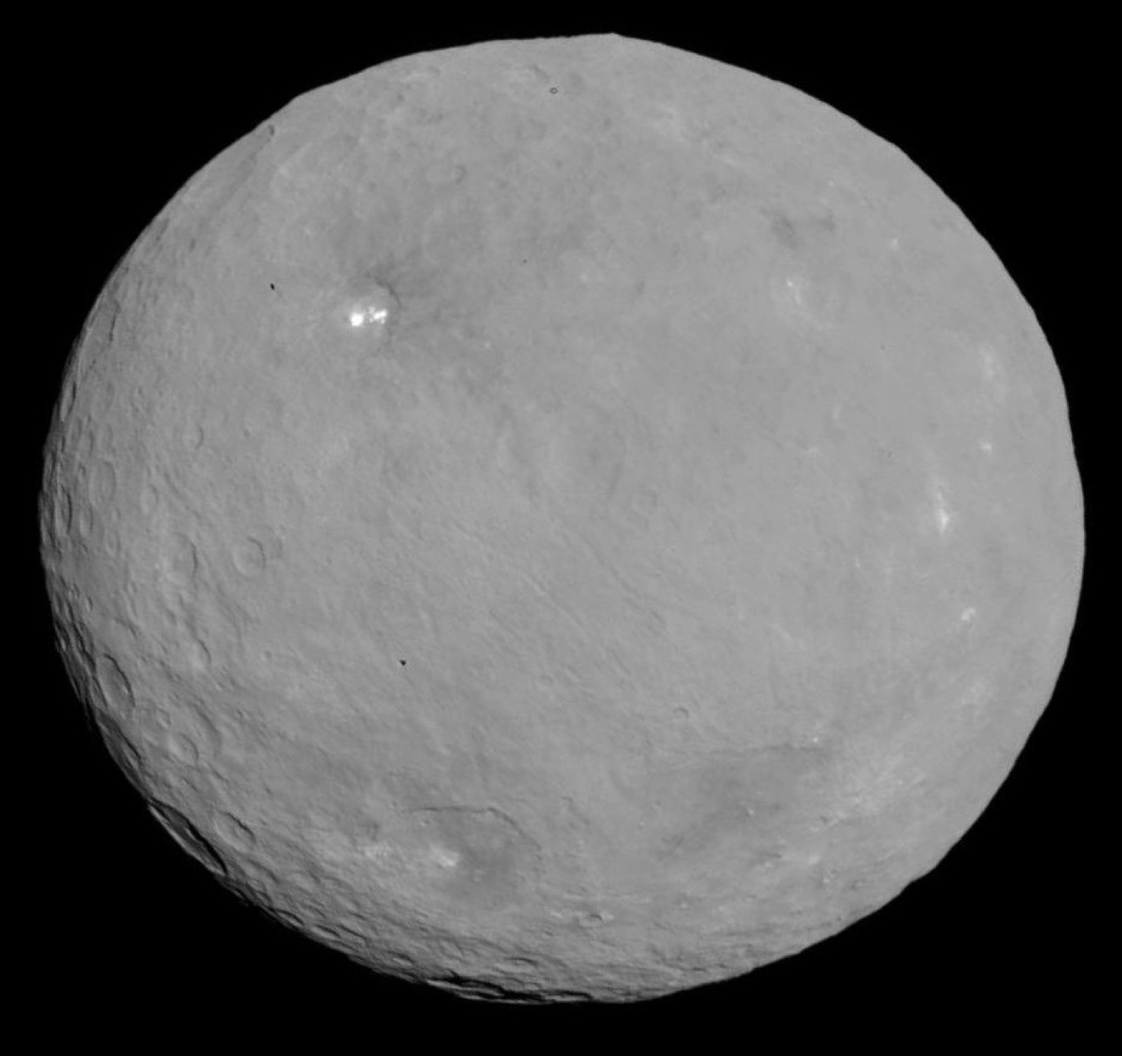 The dwarf planet Ceres, round and cratered, photographed by NASA's Dawn spacecraft, with bright pale spots in one crater.
