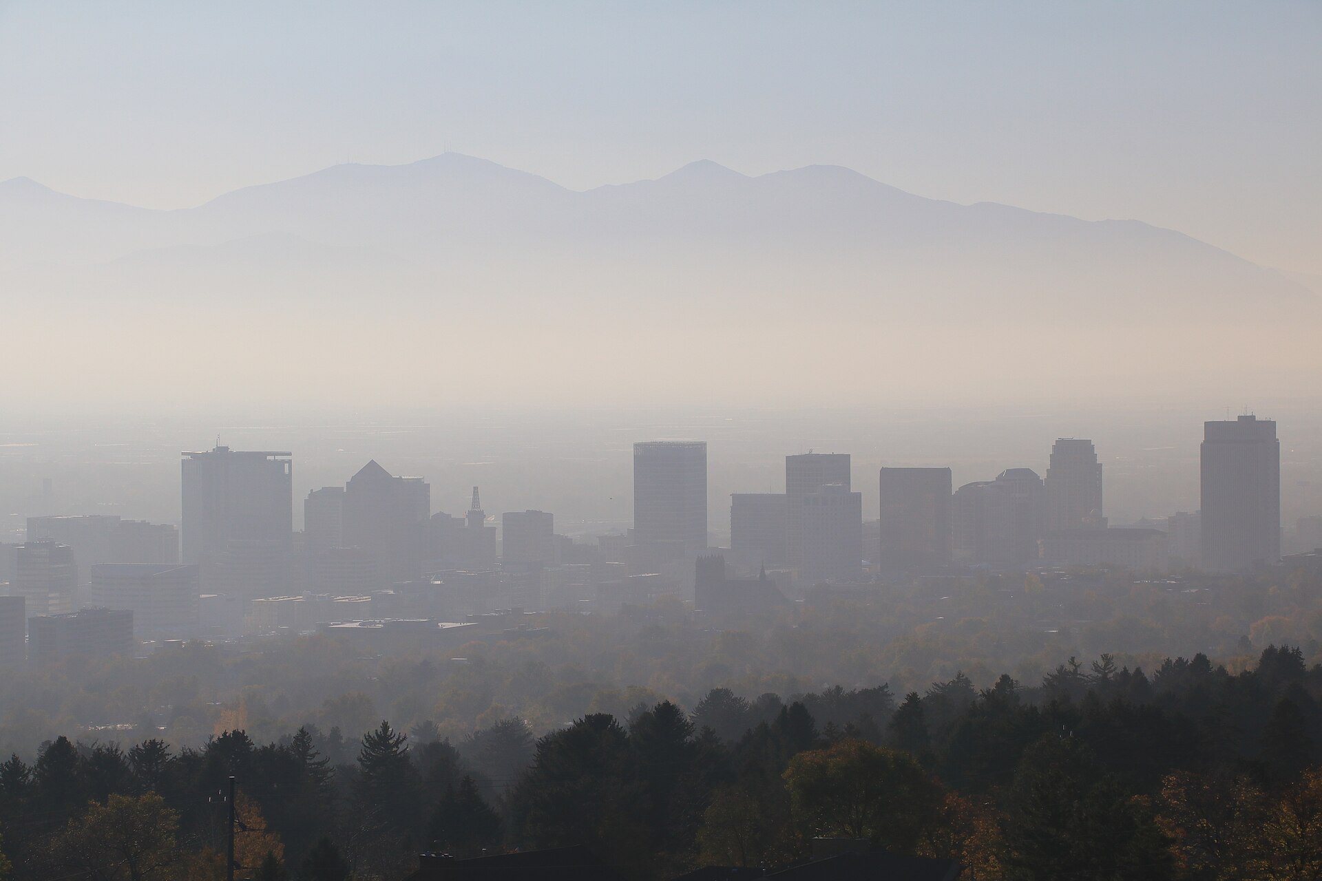 A city skyline half hidden in a thick brown haze, with mountains barely visible behind it