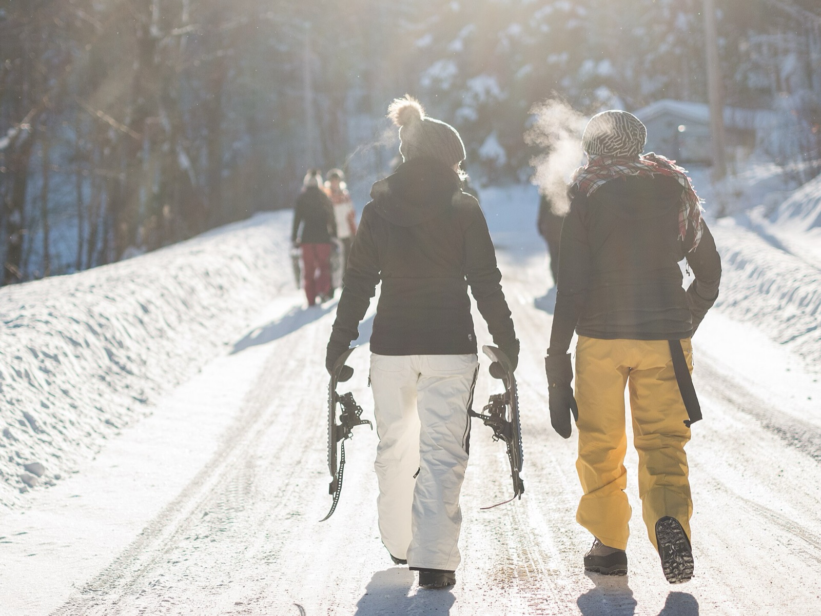 Two people walking on a snowy road on a frosty day, with a puff of warm breath showing clearly in the cold air as one of them breathes out.