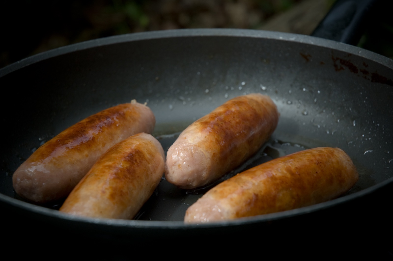 Sausages sizzling and browning in a frying pan.