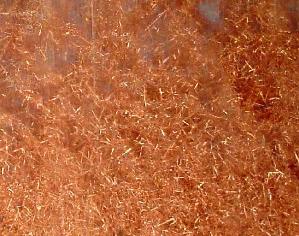 A mass of natural copper crystals catching the light in a warm metallic orange, the shine that comes from loose electrons
