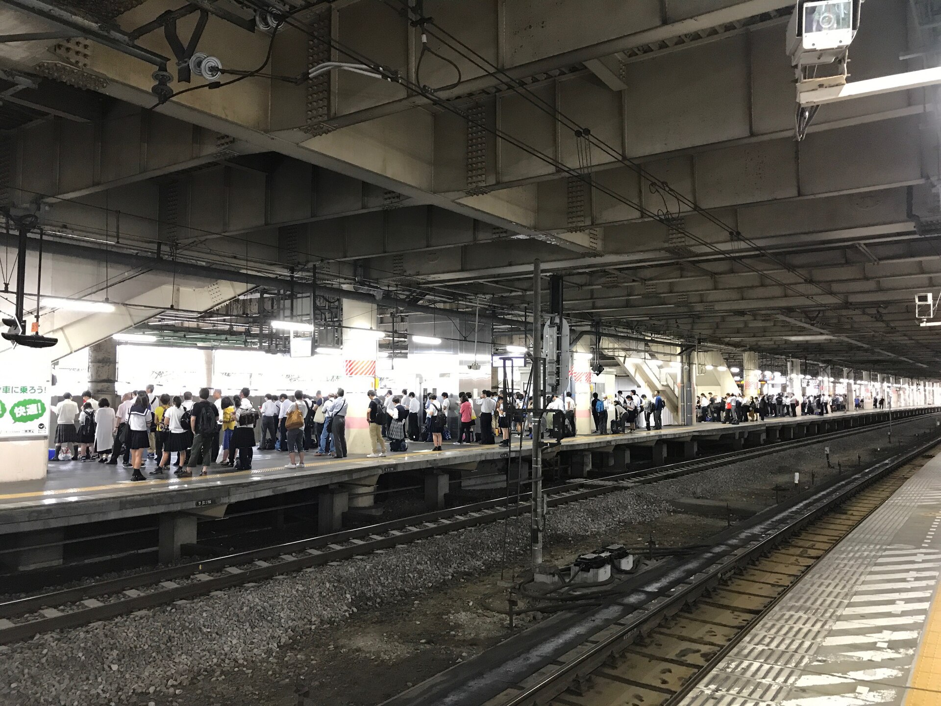 A railway platform packed with people standing shoulder to shoulder under a low roof, waiting for a train