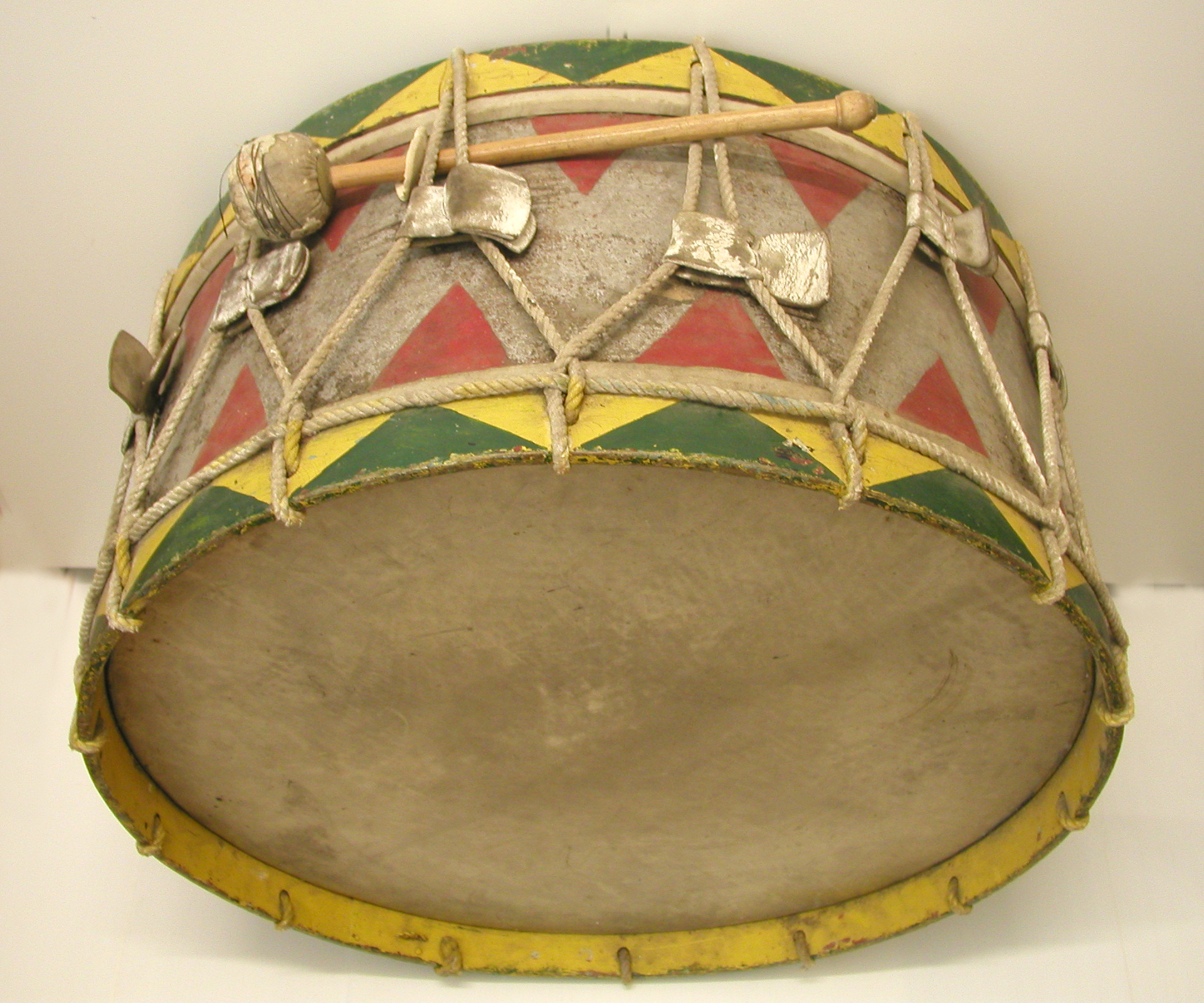 A brightly painted drum with its taut skin and a wooden beater resting on top, ropes zigzagging round the shell to pull the skin tight