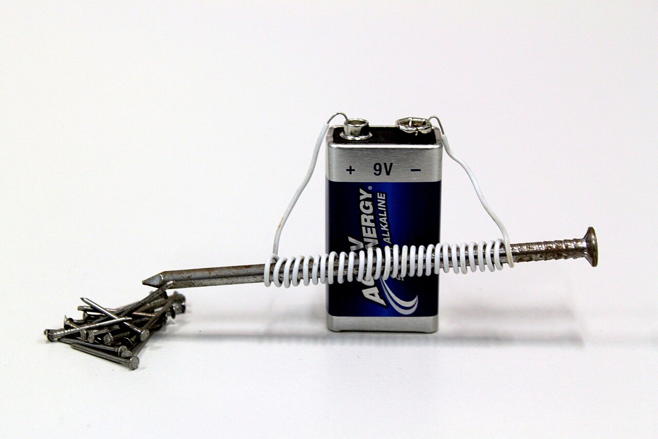 A home-made electromagnet: wire coiled around an iron nail and connected to a nine volt battery, picking up a cluster of small nails