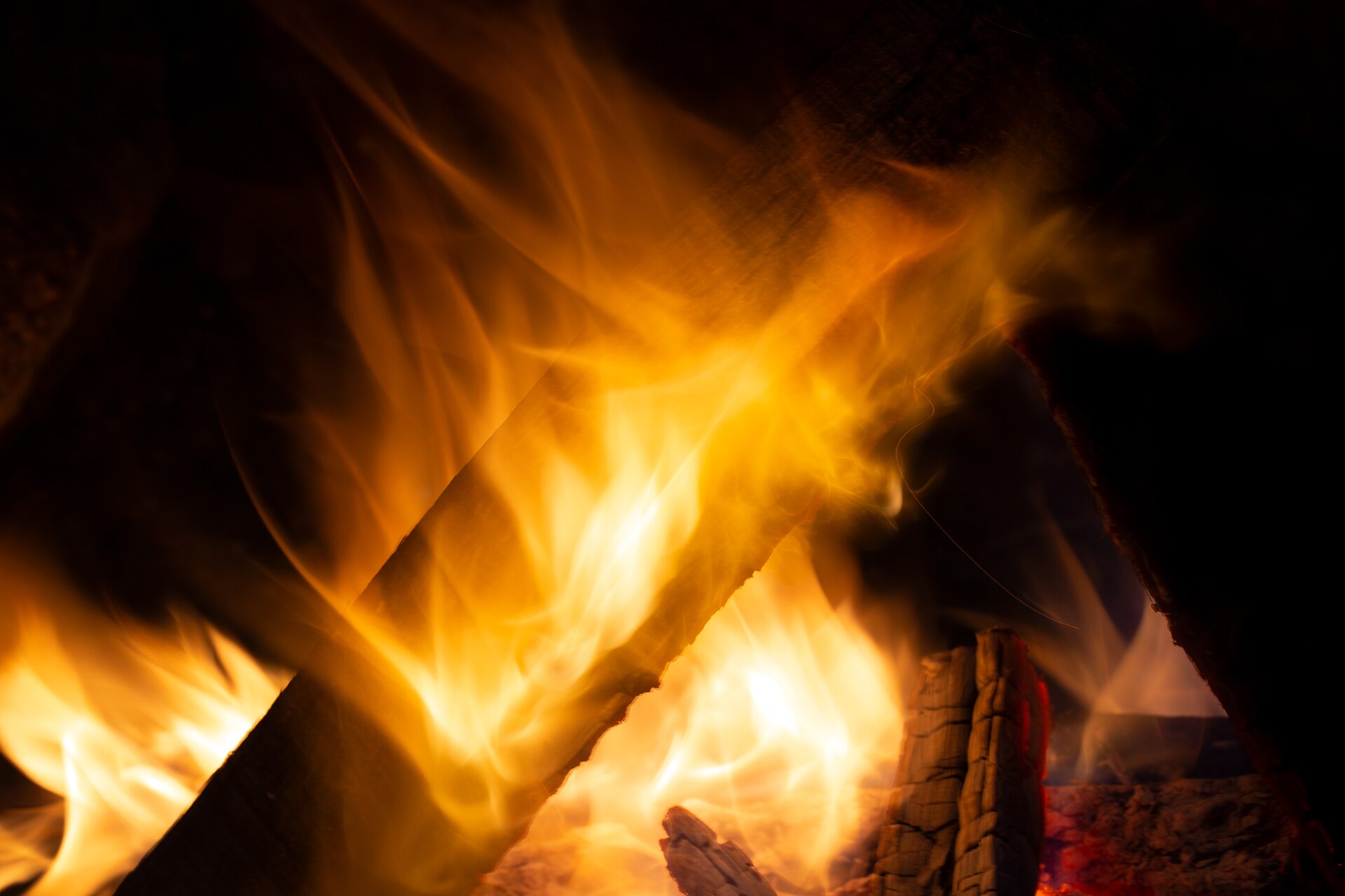 Bright orange flames leaping from a campfire, with glowing embers at the base.
