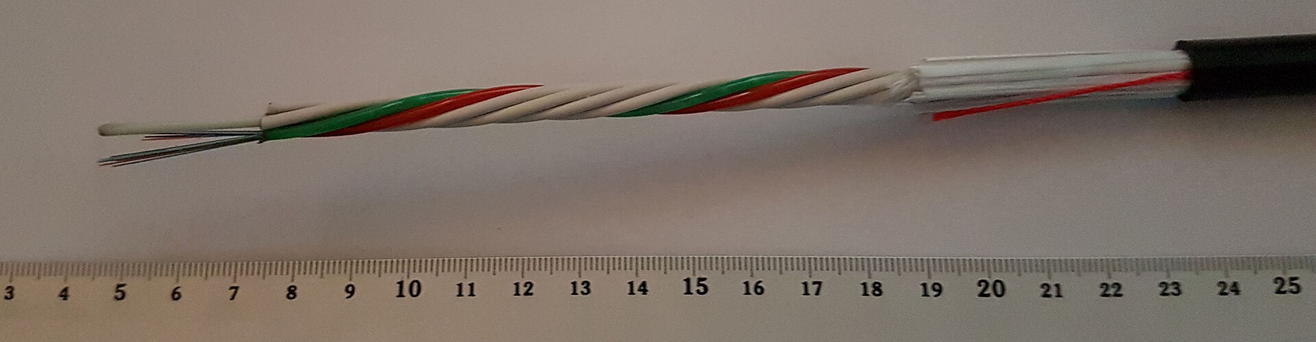 A fibre-optic cable stripped back beside a ruler, showing the hair-thin glass fibres inside their coloured coats