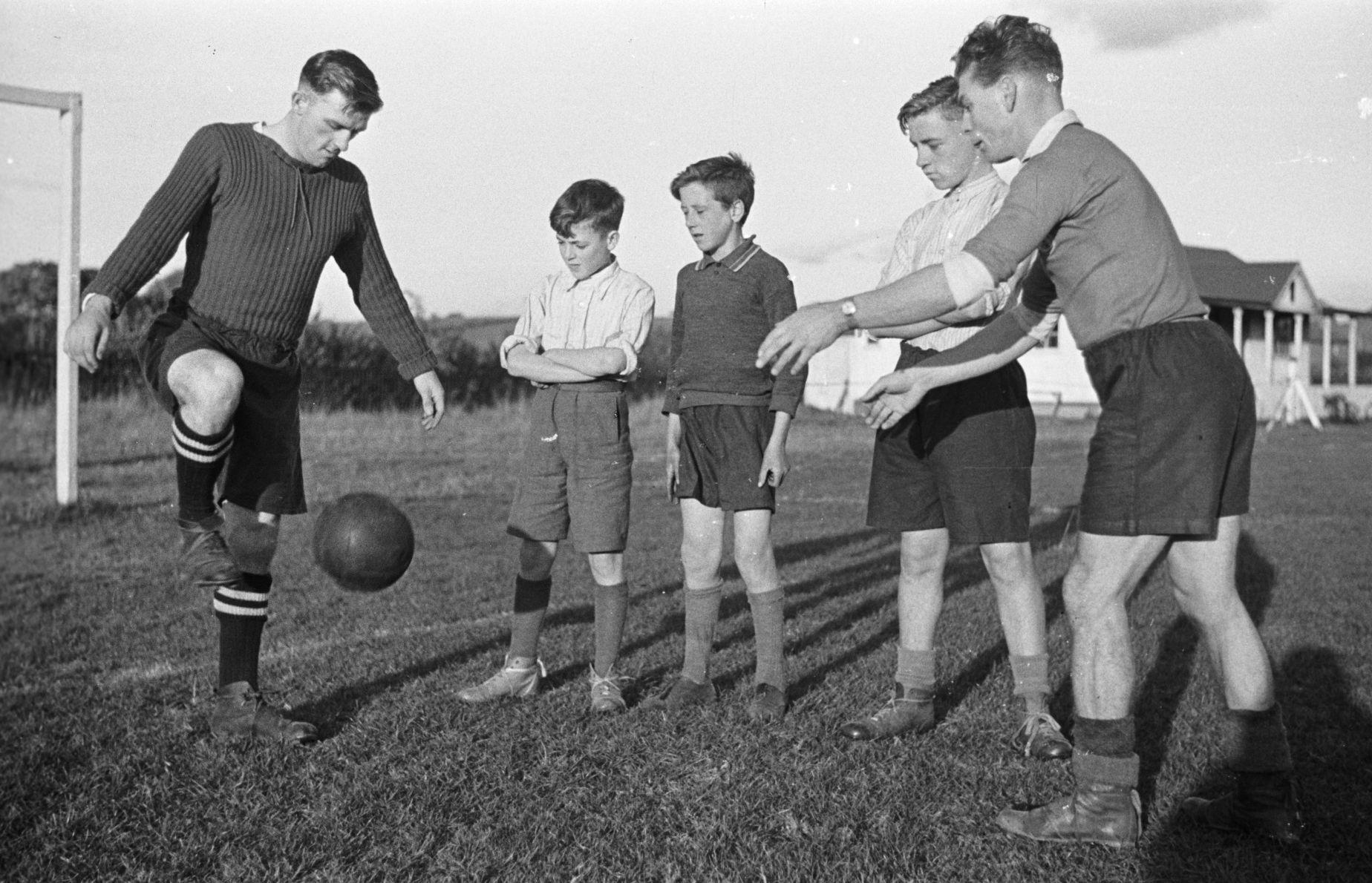 A coach showing young footballers how to control a ball at a training session on a grass pitch