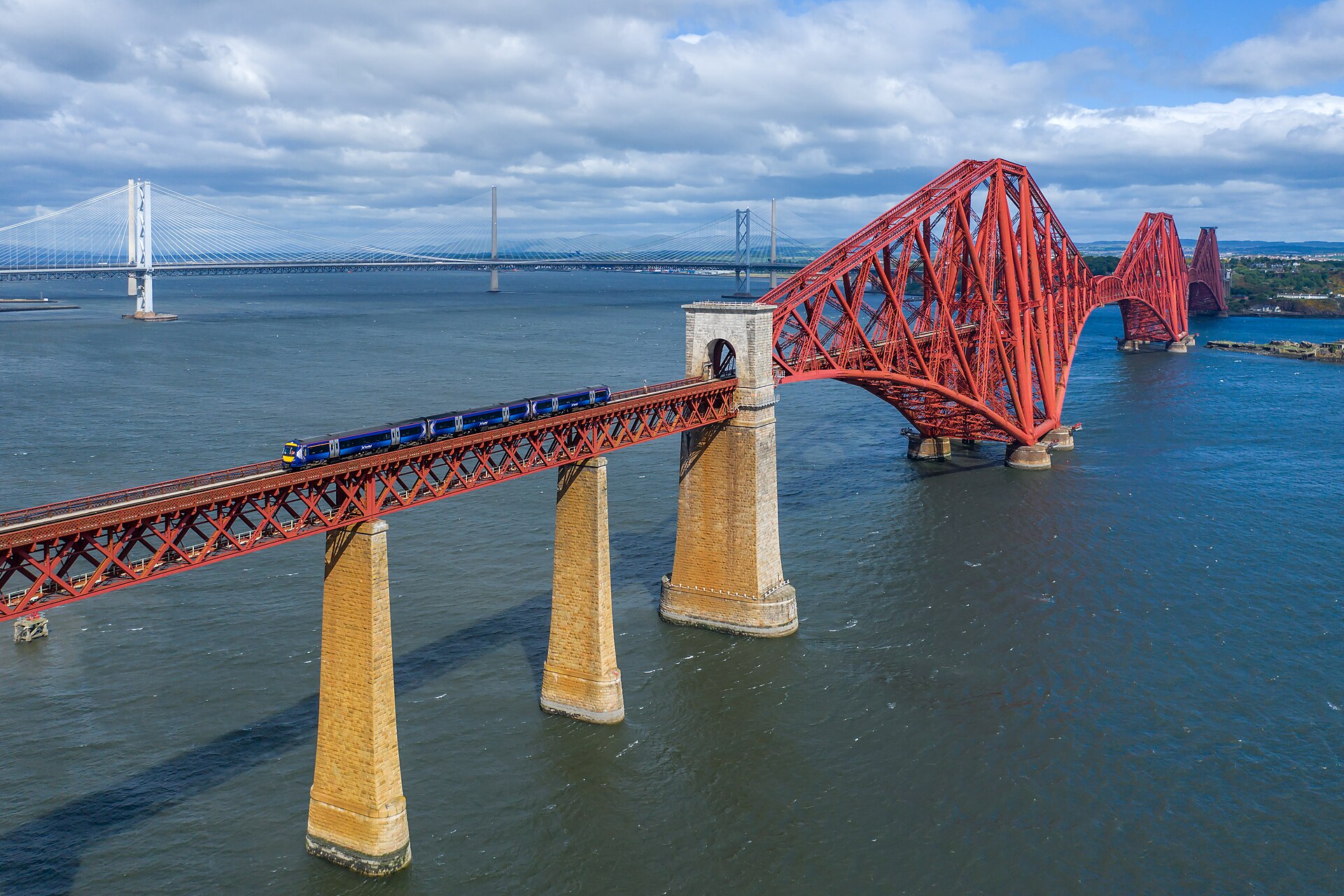 The Forth Bridge in Scotland, its huge red steelwork made up of triangle after triangle, with a train crossing high above the water