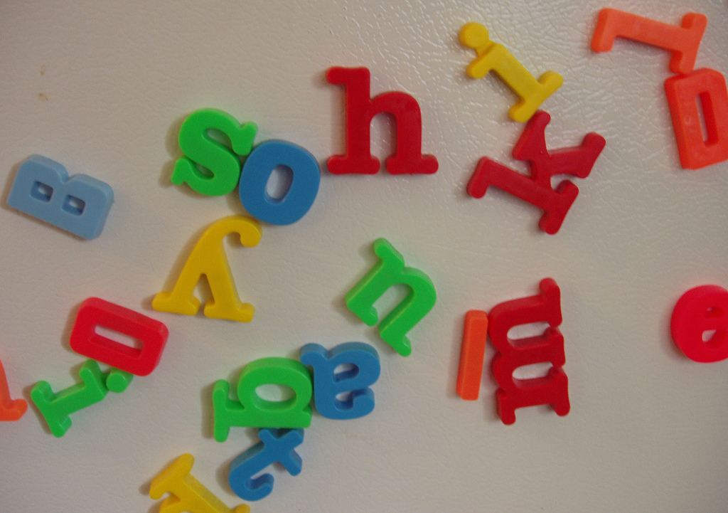 Colourful plastic magnetic letters clinging to a white fridge door