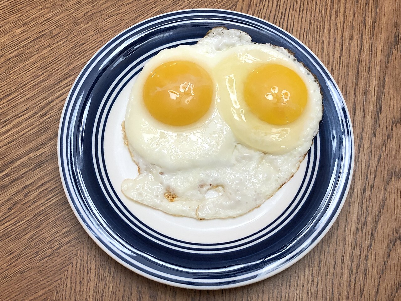 Two sunny-side up eggs on a plate, the whites cooked opaque and firm while the yolks stay glossy and round