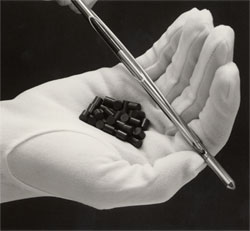 A gloved hand holding a small pile of dark nuclear fuel pellets, each one about the size of a fingertip