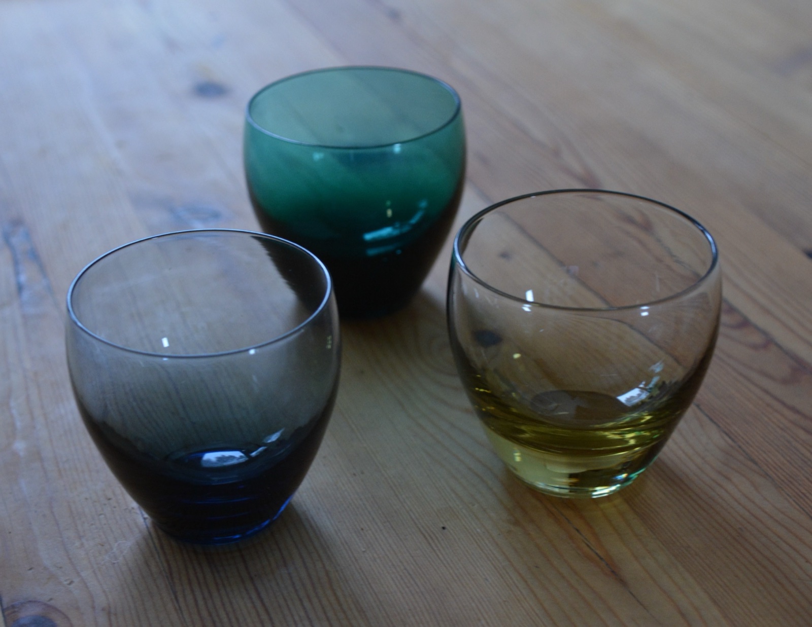 Three translucent drinking glasses on a wooden table, the grain visible through them