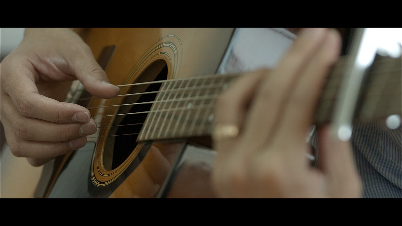 A close-up of an acoustic guitar being played, with one hand plucking the strings over the sound hole