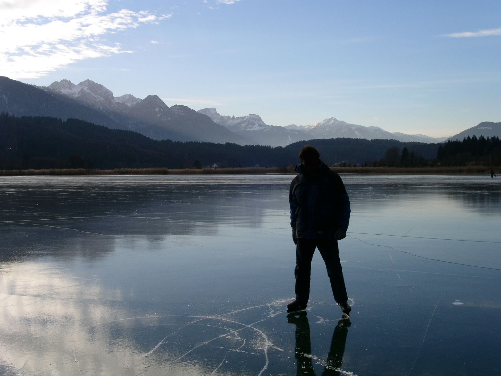A person standing on the smooth, gleaming ice of a frozen mountain lake.