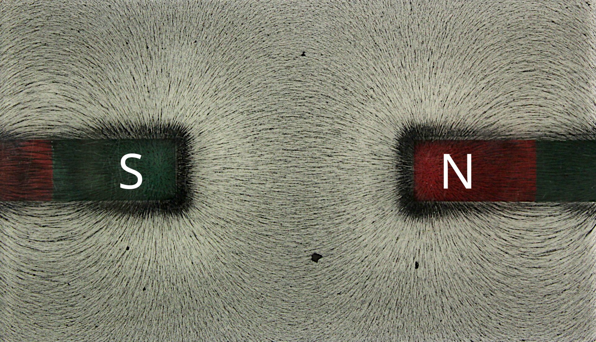Iron filings drawn into sweeping curves between the north and south poles of two bar magnets, tracing the invisible field