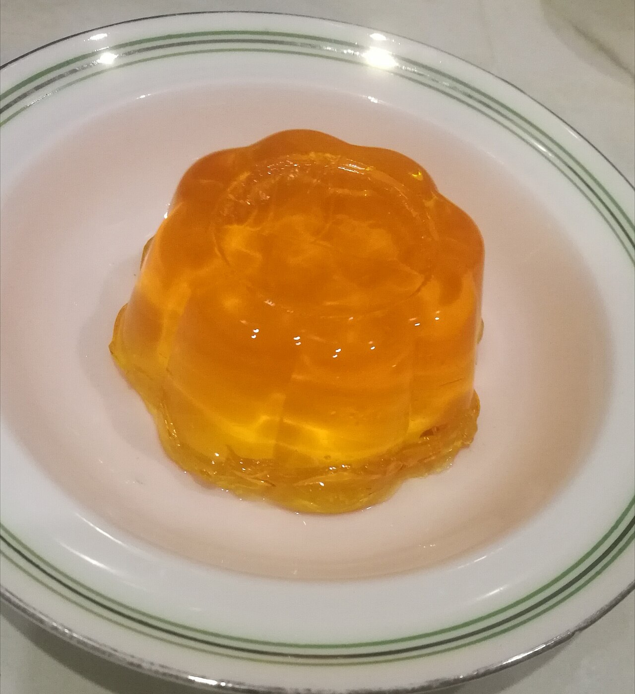 A small orange jelly turned out of its mould onto a white plate, holding its ridged shape