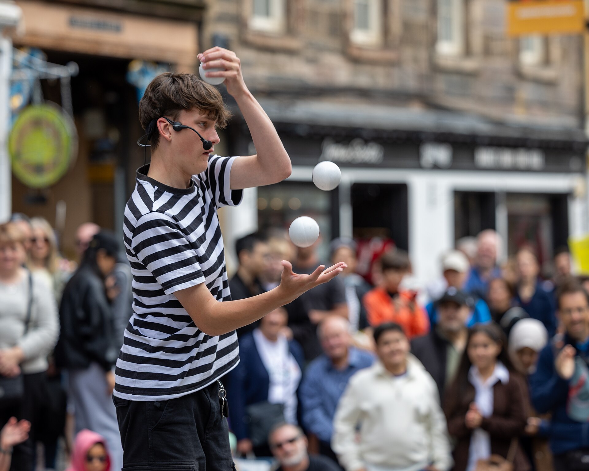 A street juggler at the Edinburgh Fringe mid-throw, three balls hanging in the air, a skill that once felt impossible