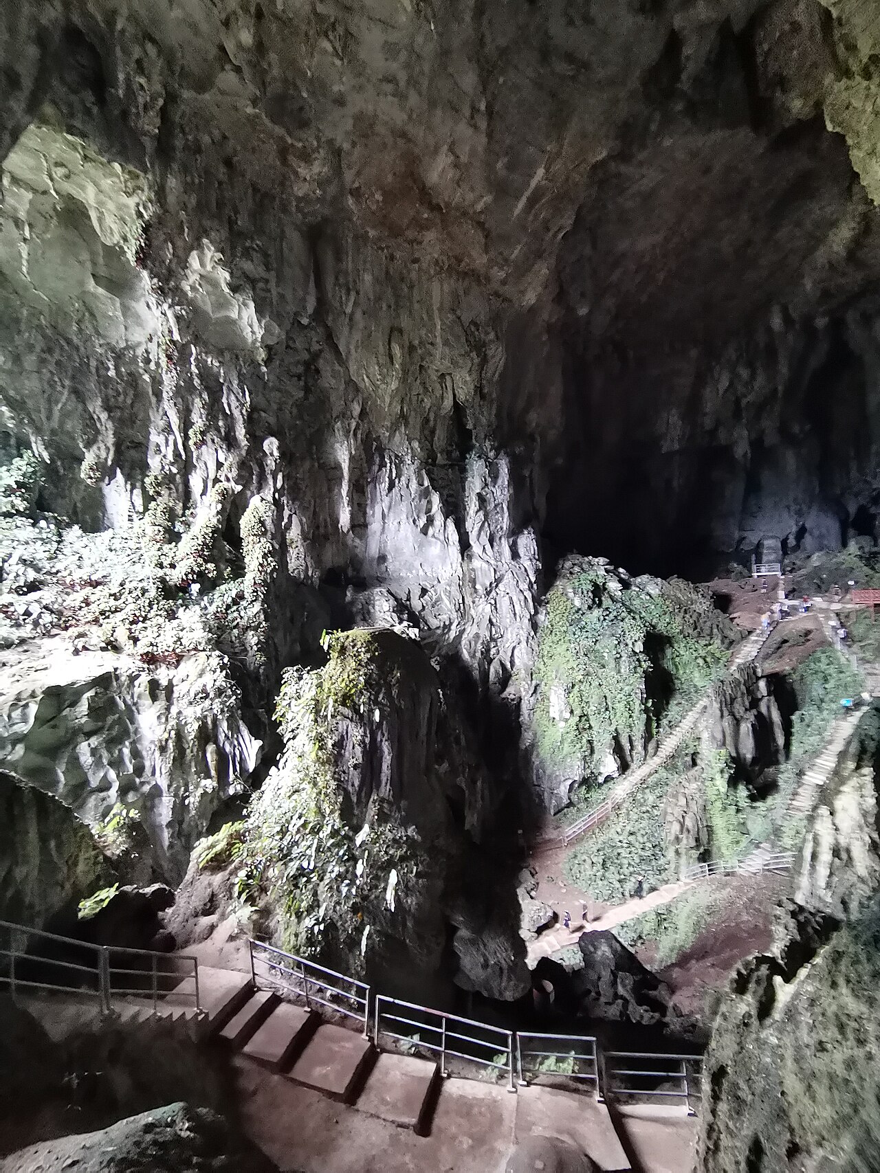 A vast underground limestone chamber with pale rock walls and hanging formations, lit from below