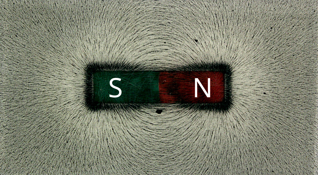 Iron filings arranged in curved lines around a bar magnet, clustering thickly at the north and south ends