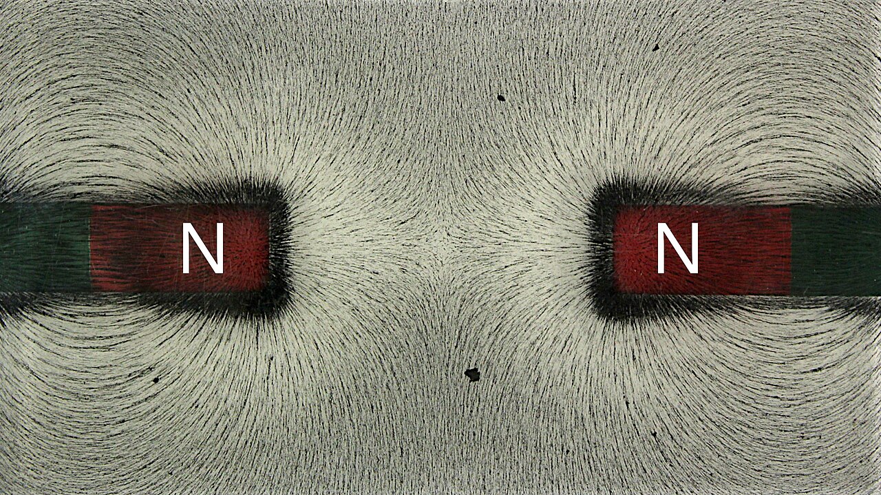 Iron filings showing the fields of two bar magnets with matching north ends facing each other, the lines curving apart in the gap between them
