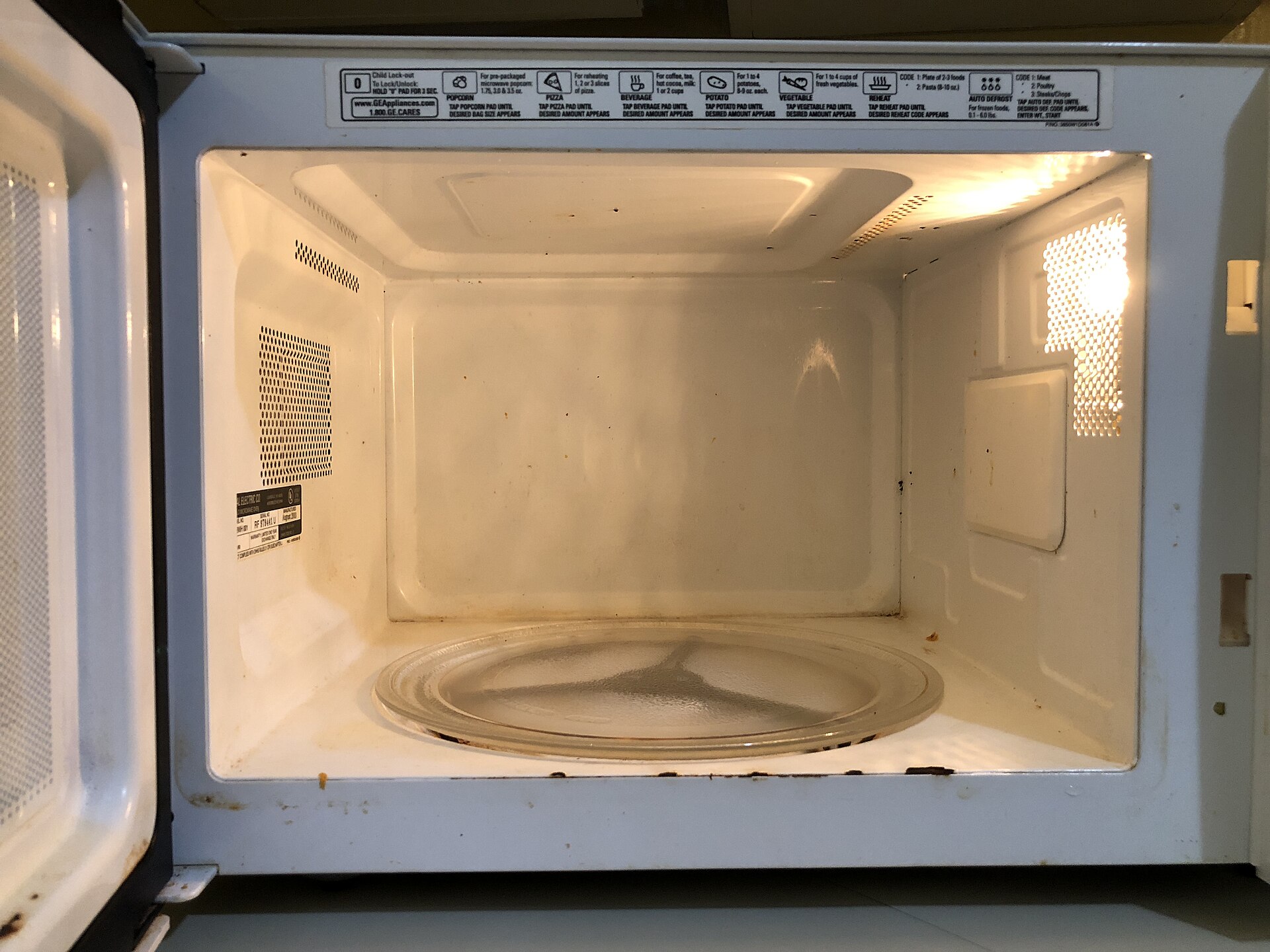 The inside of a microwave oven with its glass turntable, and the metal mesh window in the door that keeps the waves in