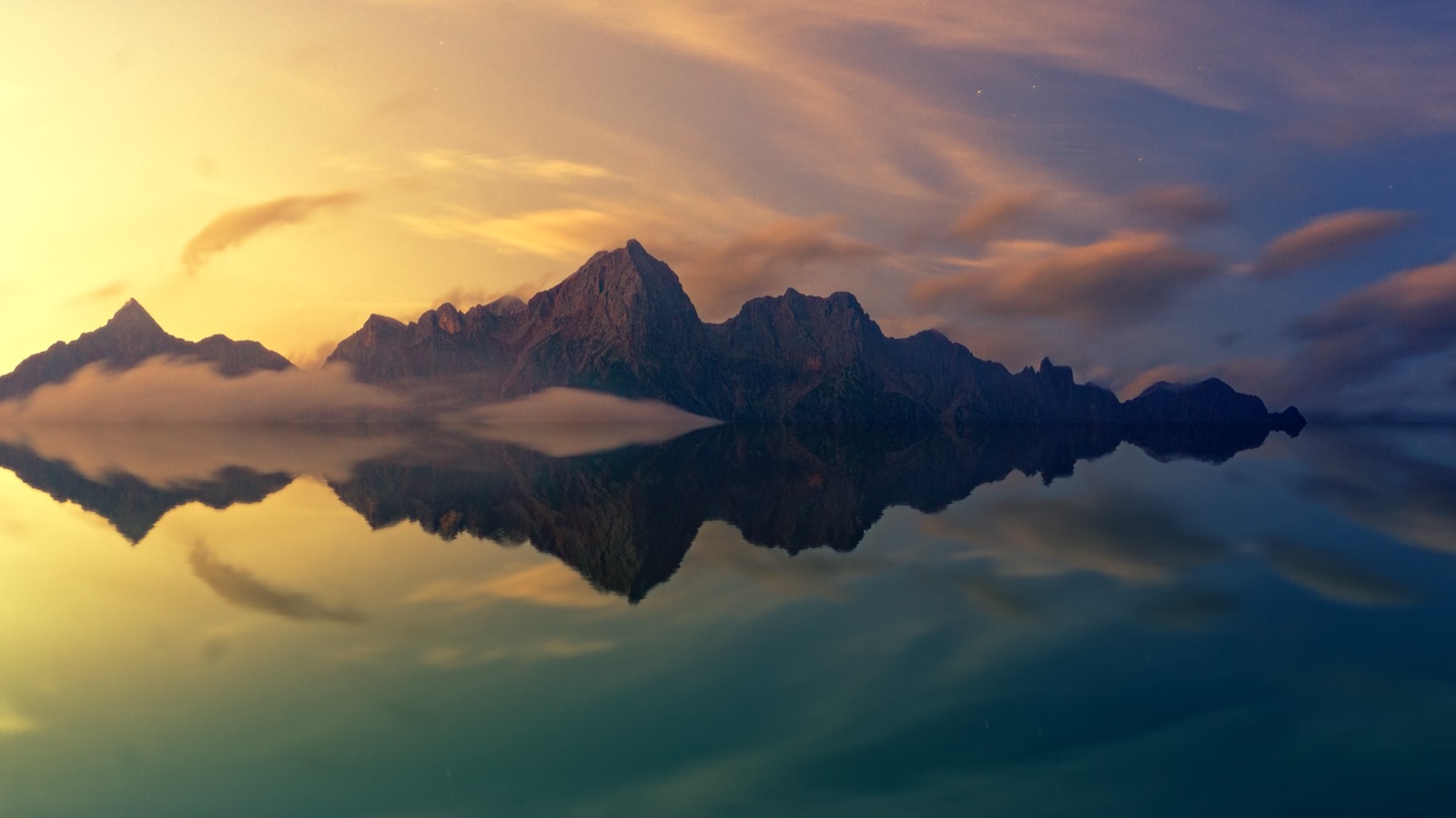 A mountain landscape mirrored perfectly in the still, smooth surface of a lake at golden light.