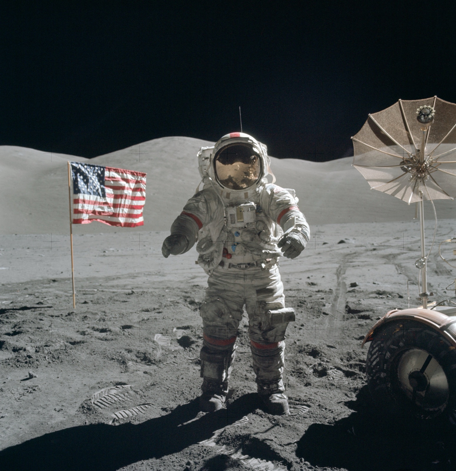 An Apollo astronaut standing on the airless surface of the Moon, with the lunar rover and flag nearby