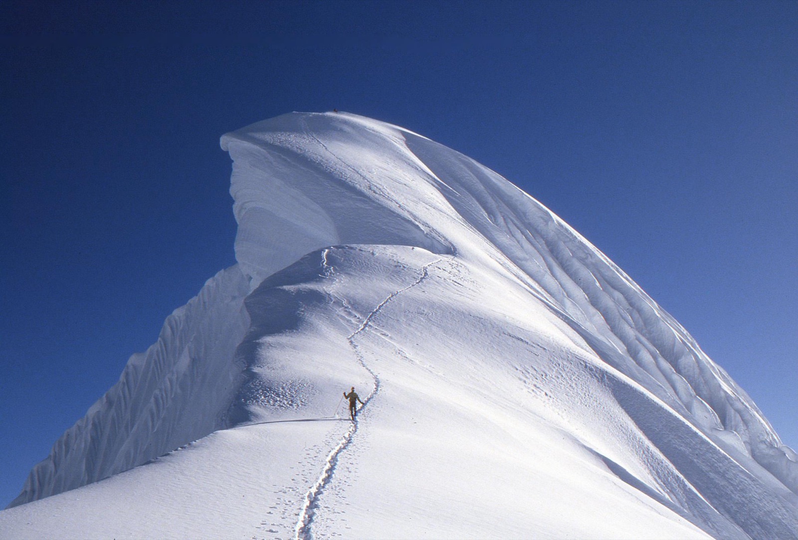 A climber on a high, snowy mountain ridge where the air is thin.