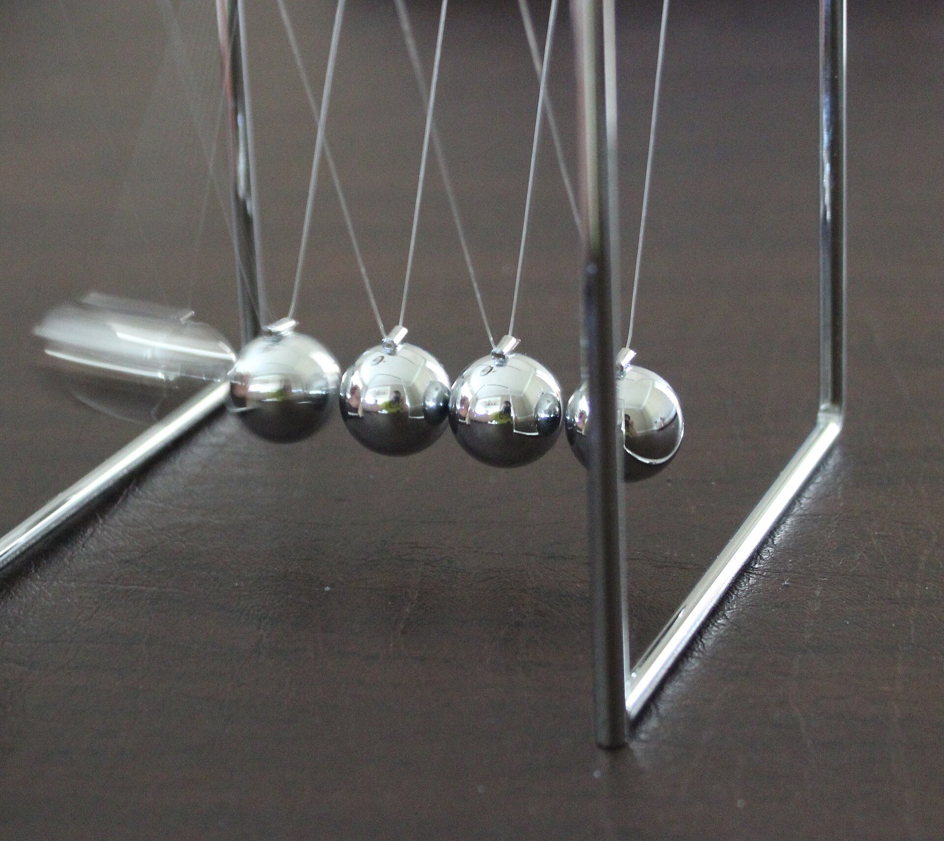 A Newton's cradle on a desk: five polished steel balls hanging in a row from thin wires, with the ball at one end swung out to the side.
