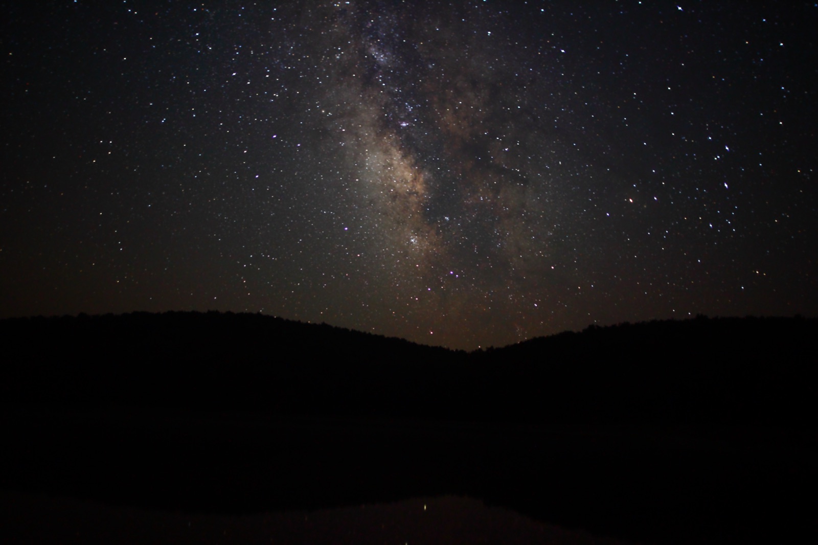The Milky Way arching over dark silhouetted hills in a mostly black night sky