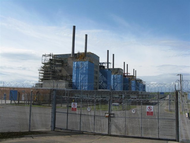 A British nuclear power station standing low and grey behind farmland, its reactor buildings squat against the sky