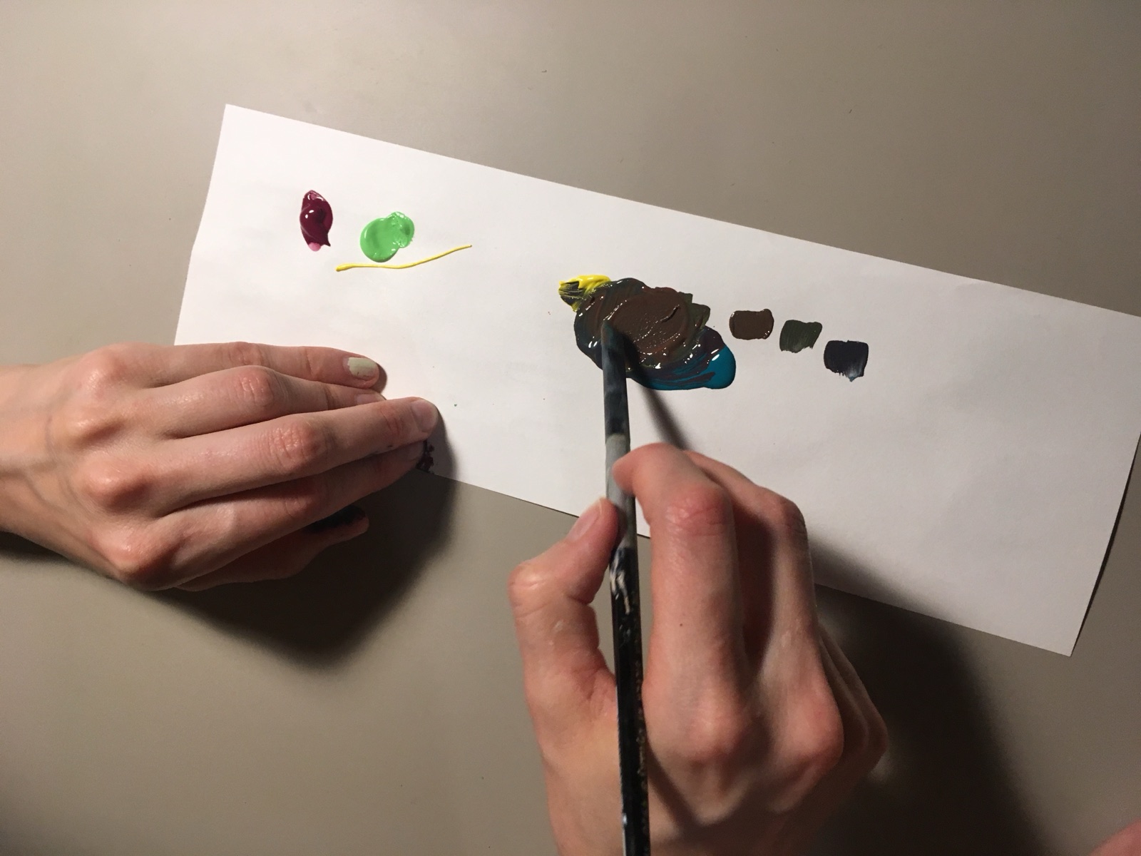 Bright red, yellow and blue paints being mixed with a brush into muddy brown swatches.