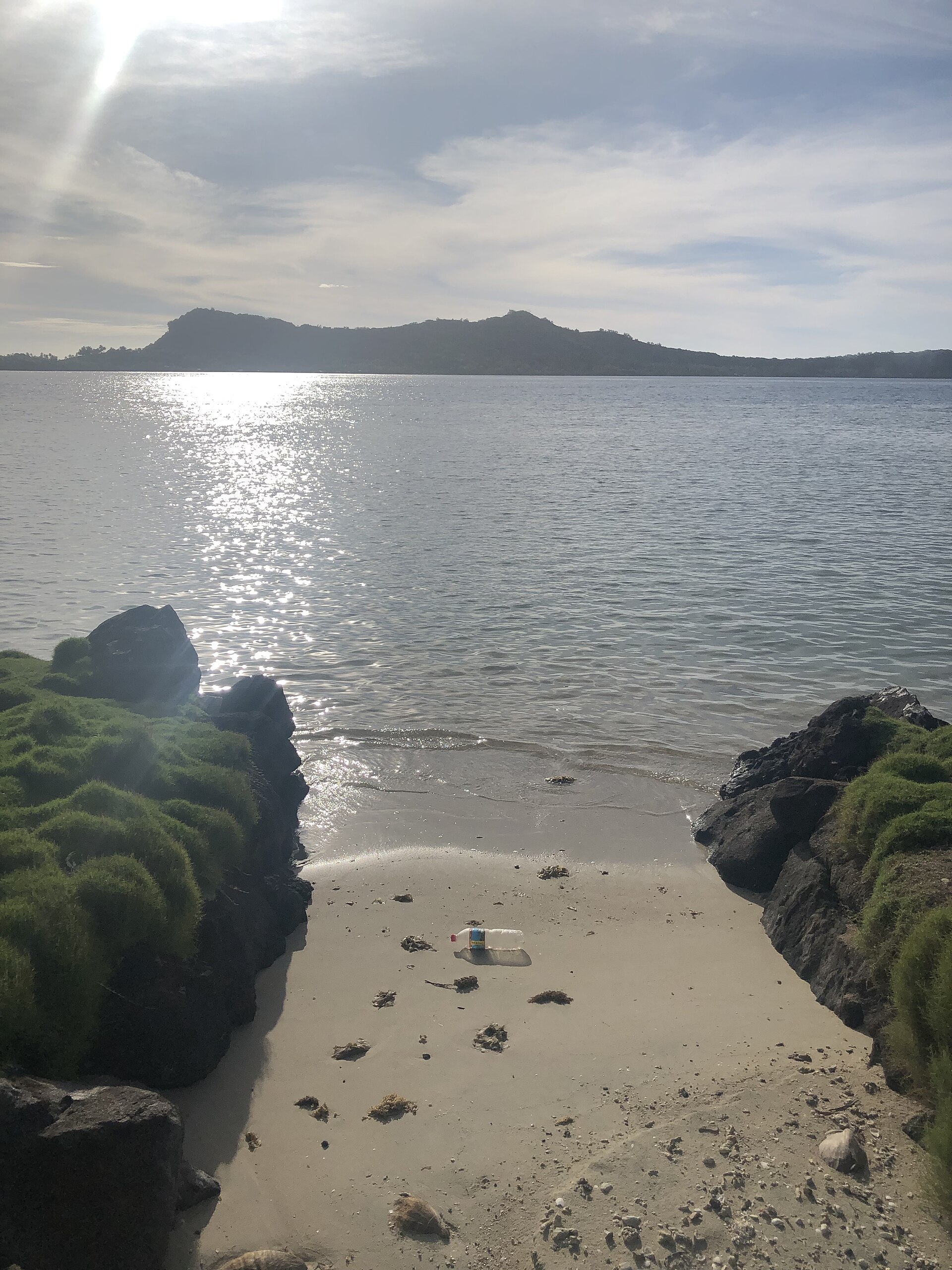 A single discarded plastic bottle lying on an otherwise clean sandy beach beside calm water.