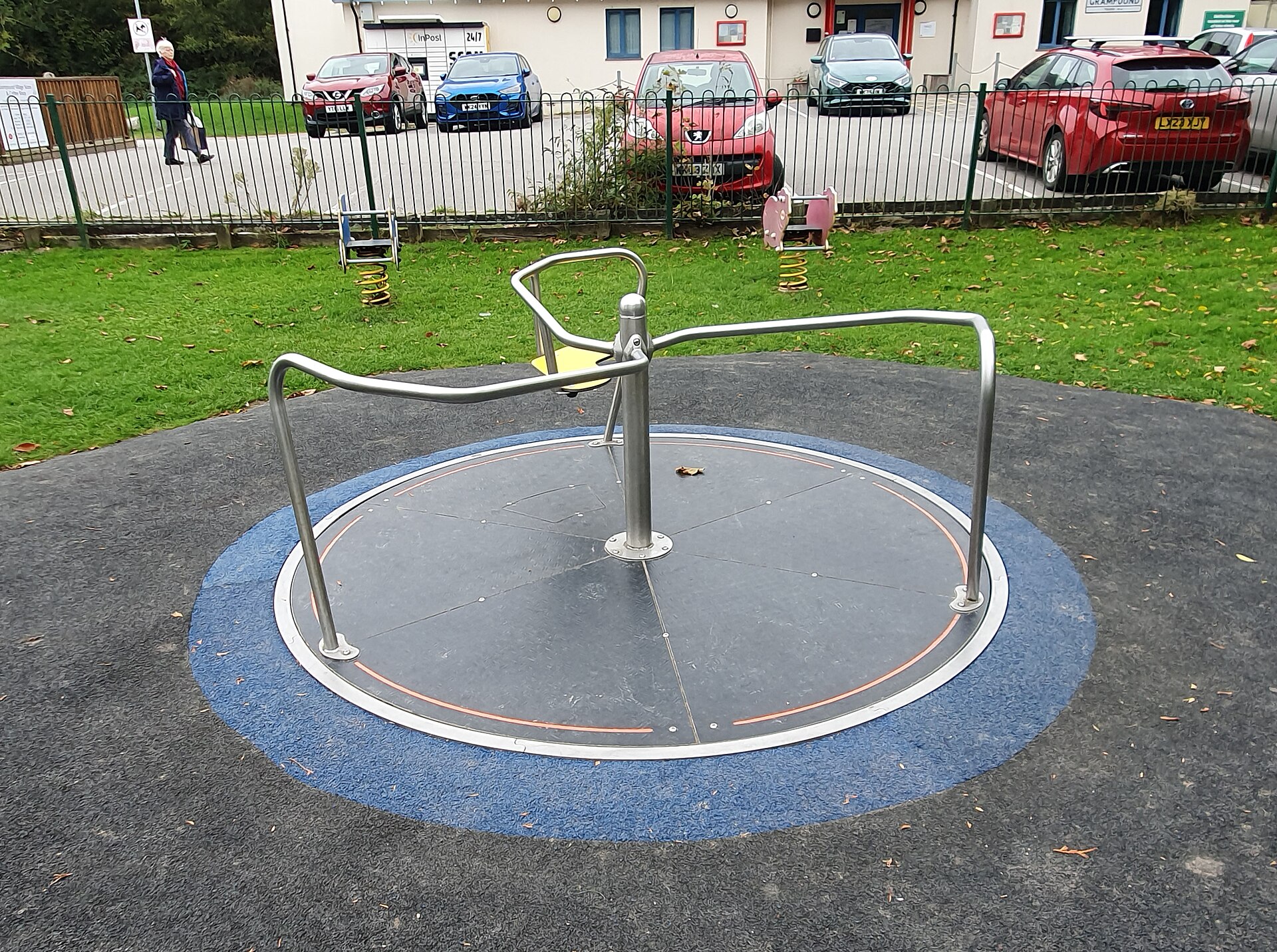 A metal playground roundabout on a rubber safety surface, with curved handrails around a flat spinning disc.