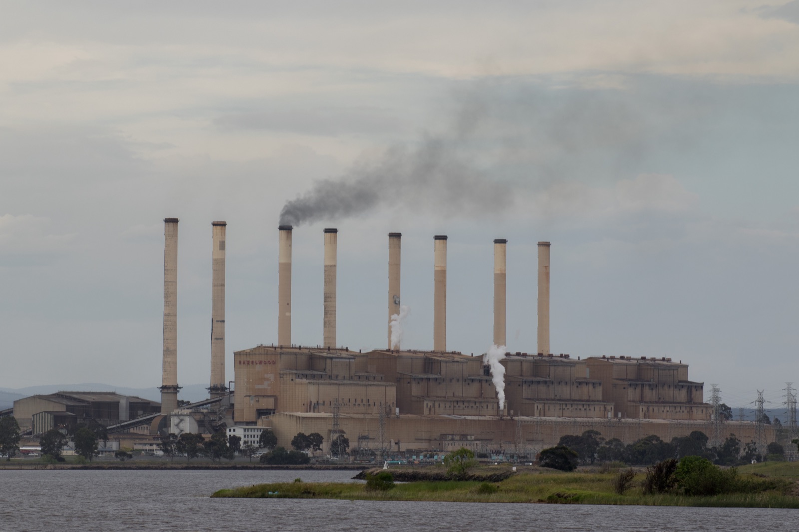 A coal-fired power station with tall chimneys, one sending up a dark plume of smoke.