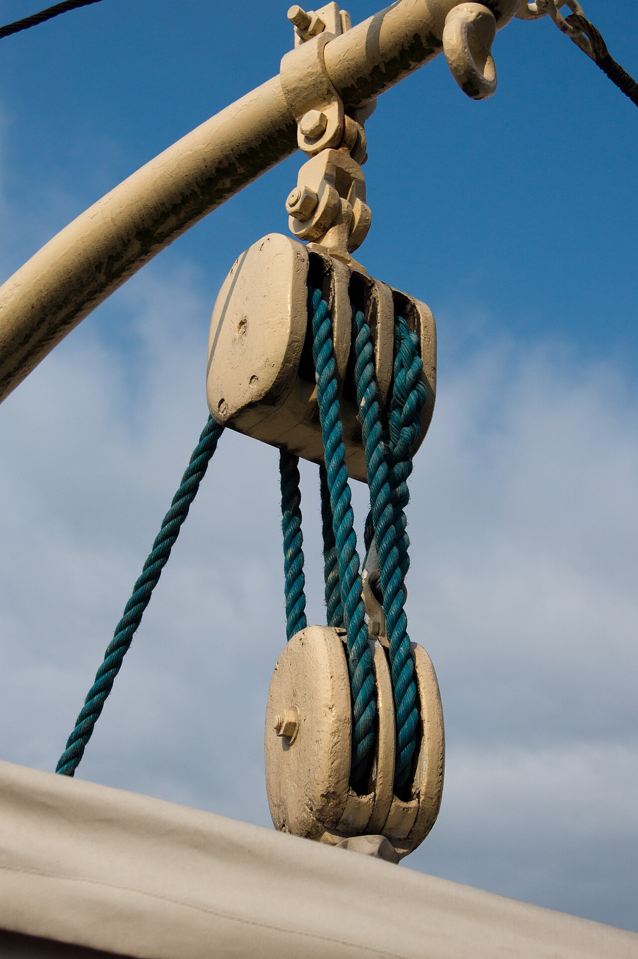 A block and tackle against a blue sky, with rope wound several times between an upper and a lower set of pulley wheels