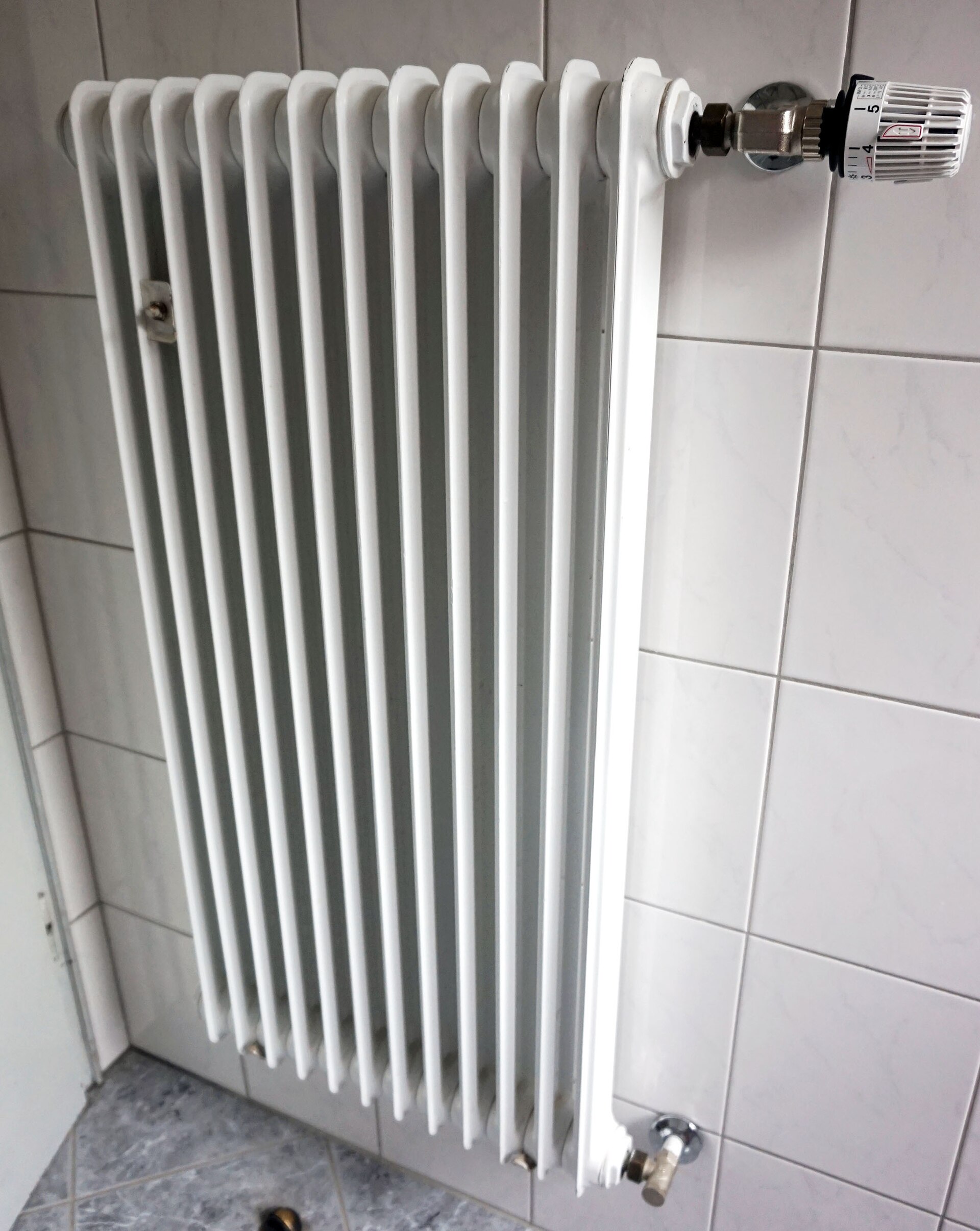 A white column radiator mounted on a tiled wall, with a numbered thermostatic valve at one end.