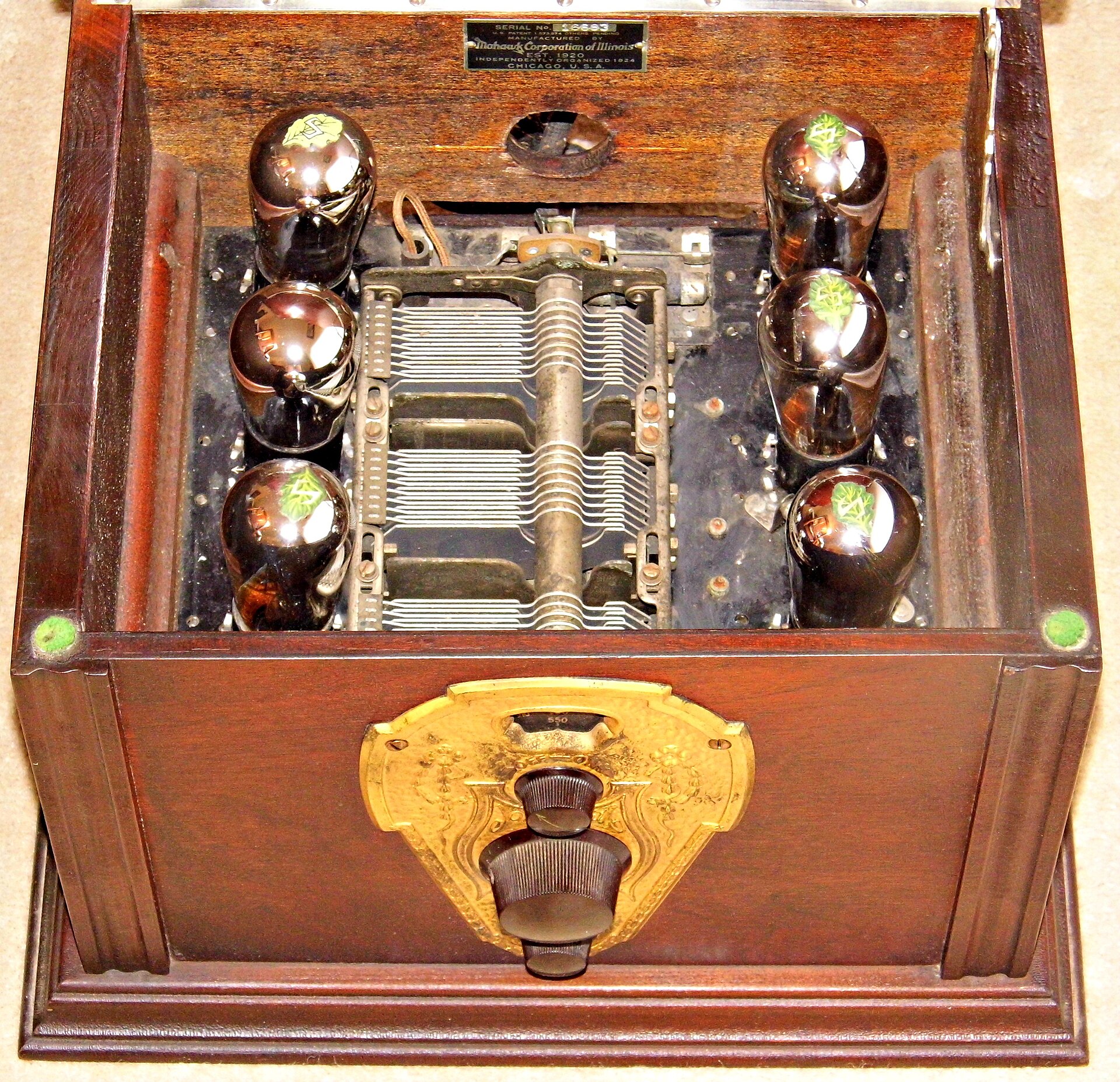 The inside of a 1920s valve radio with its lid open, showing glass valves and the fanned metal plates of the variable capacitor used to tune it, above a brass tuning dial.