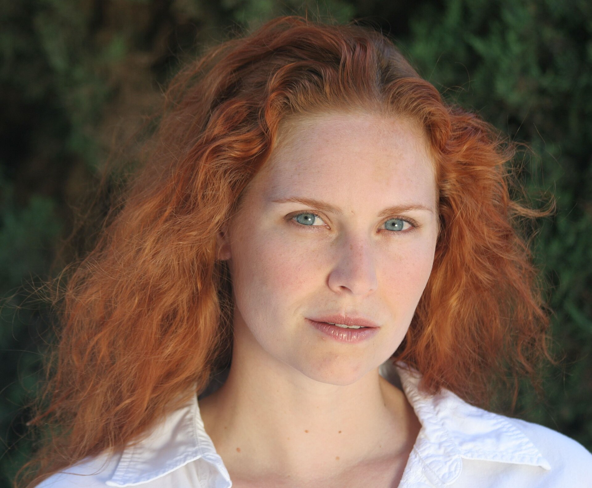 A portrait of a woman with bright coppery red curly hair and freckled pale skin.